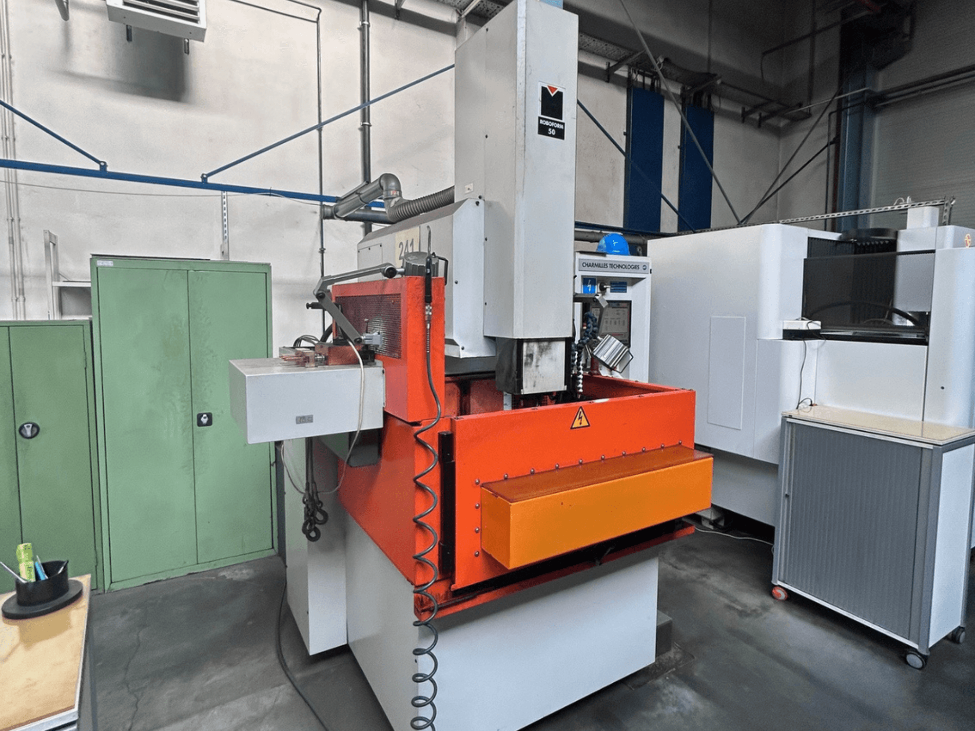 Вид спереди на станок CHARMILLES ROBOFORM 50 Die-Sinking EDM Machine с оранжевой панелью, интерфейсом управления и окружающим оборудованием.
