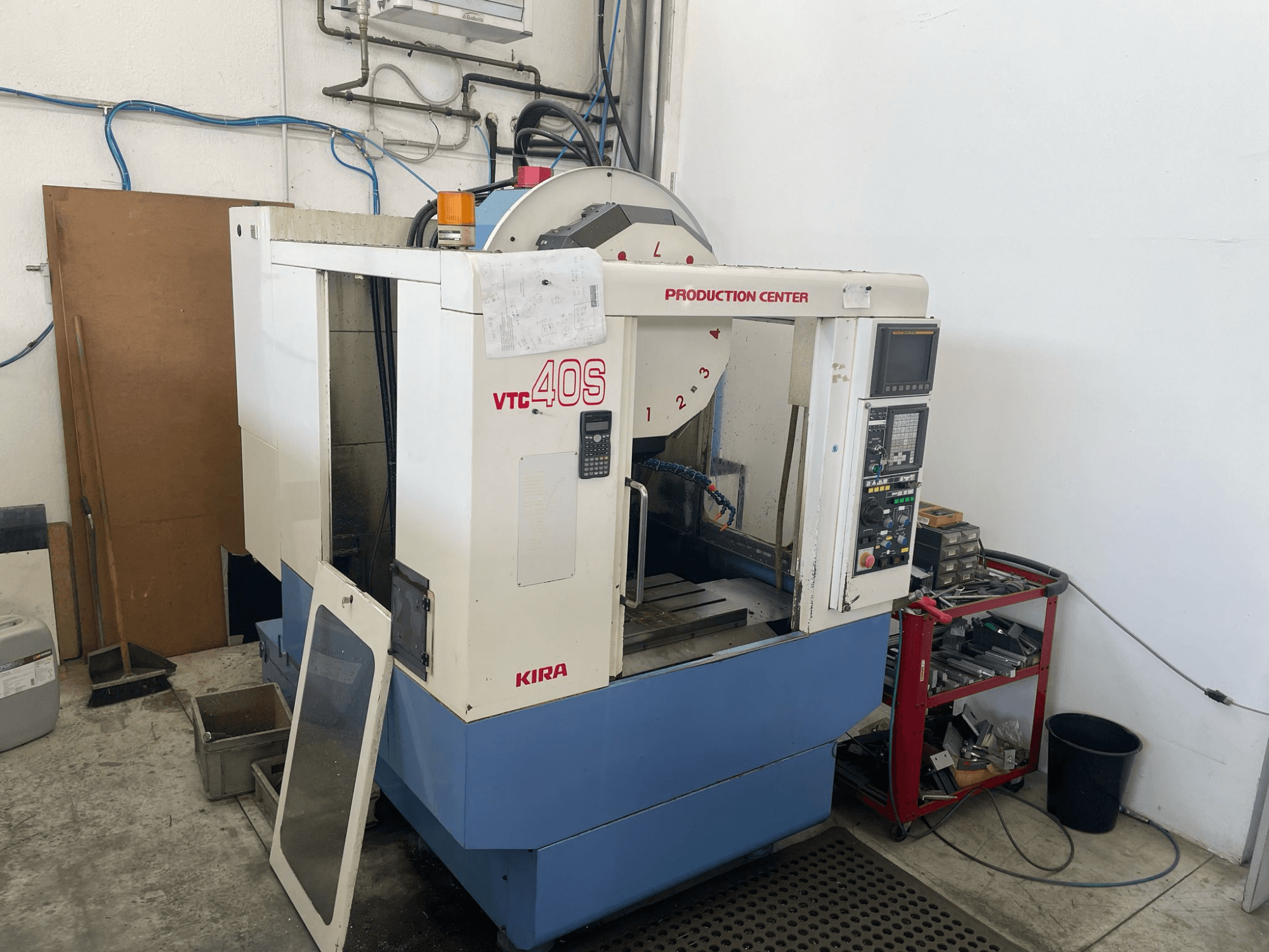 Обрабатывающий центр KIRA VTC 40S вид сбоку, панель управления, открытая дверь, инструменты на тележке для хранения.