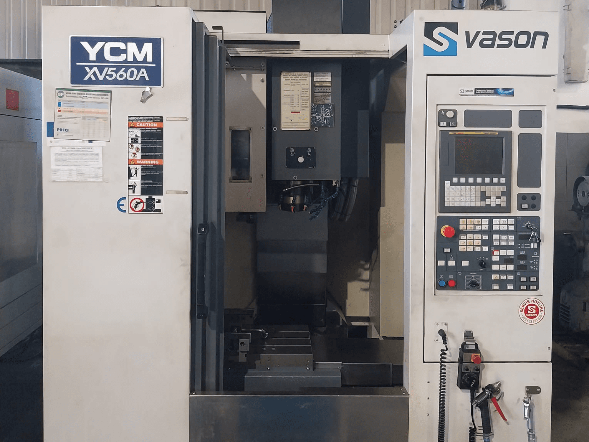 Вид спереди вертикального обрабатывающего центра YCM XV 560A с панелью управления и рабочим столом, на котором видны обрабатываемые детали.