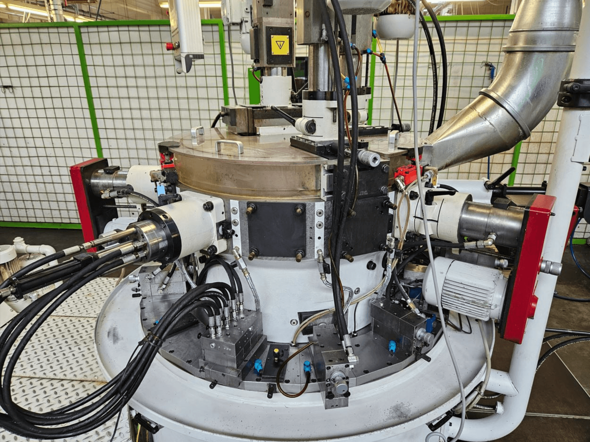 Крупный план промышленной машины с гидравлическими шлангами, металлическими деталями и вращающимся основанием. Бренд не виден.