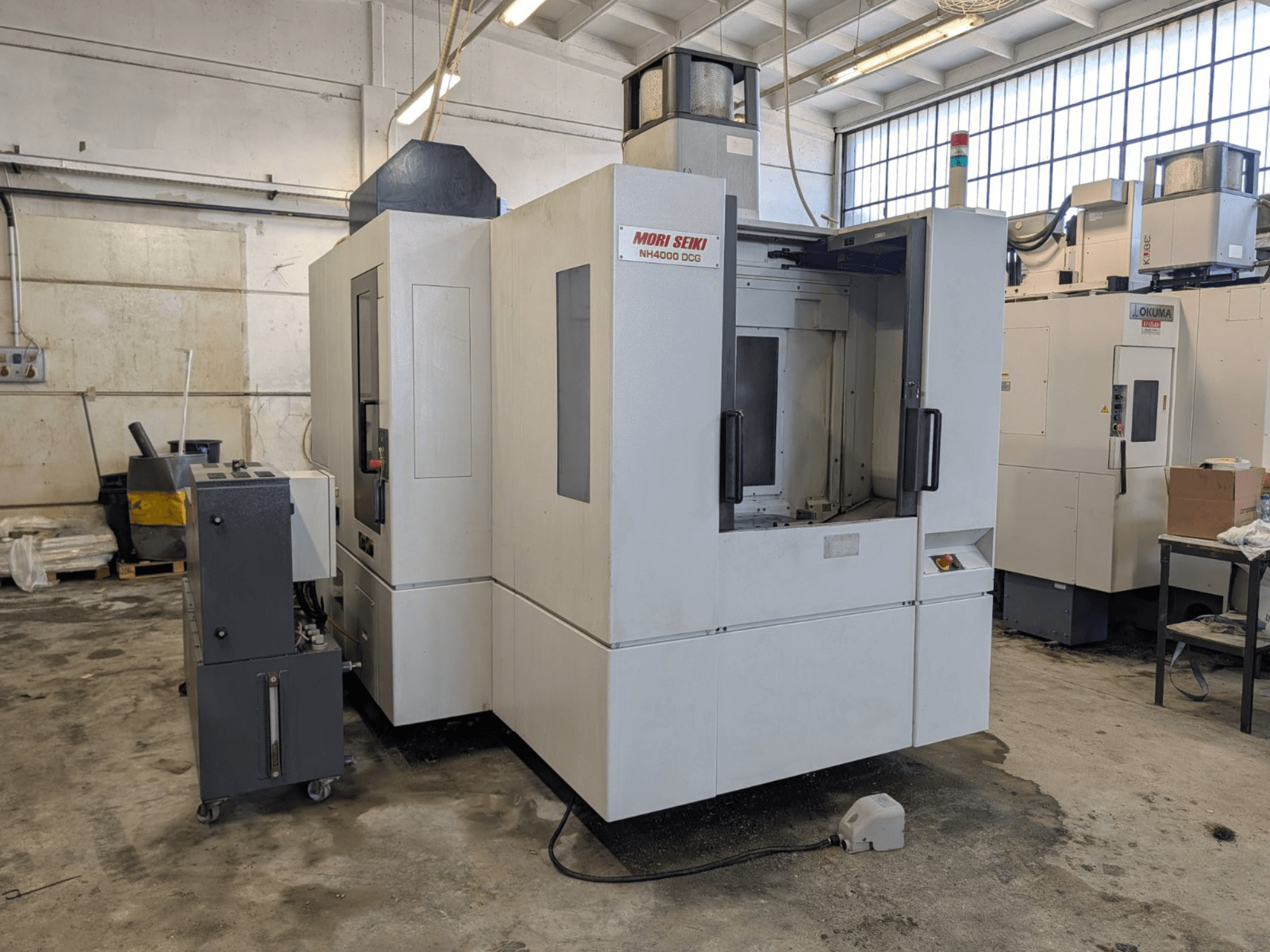 Горизонтальный обрабатывающий центр MORI SEIKI NH 4000 DCG, вид спереди, демонстрирует панель управления и рабочую зону, серо-белая отделка.