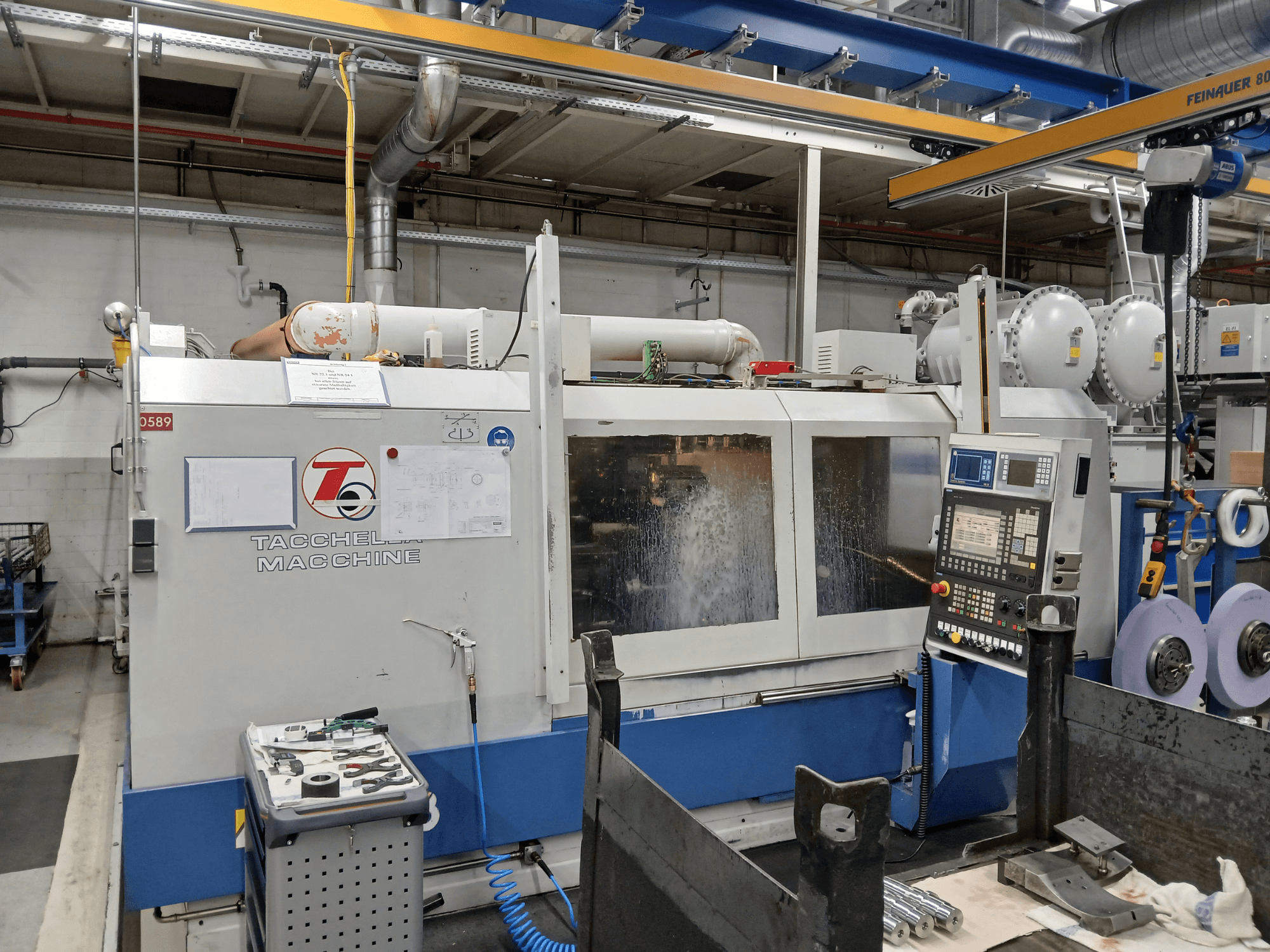 Обрабатывающий центр Tacchella спереди, видны панель управления и инструменты. Во время работы распыляется водяная охлаждающая жидкость.