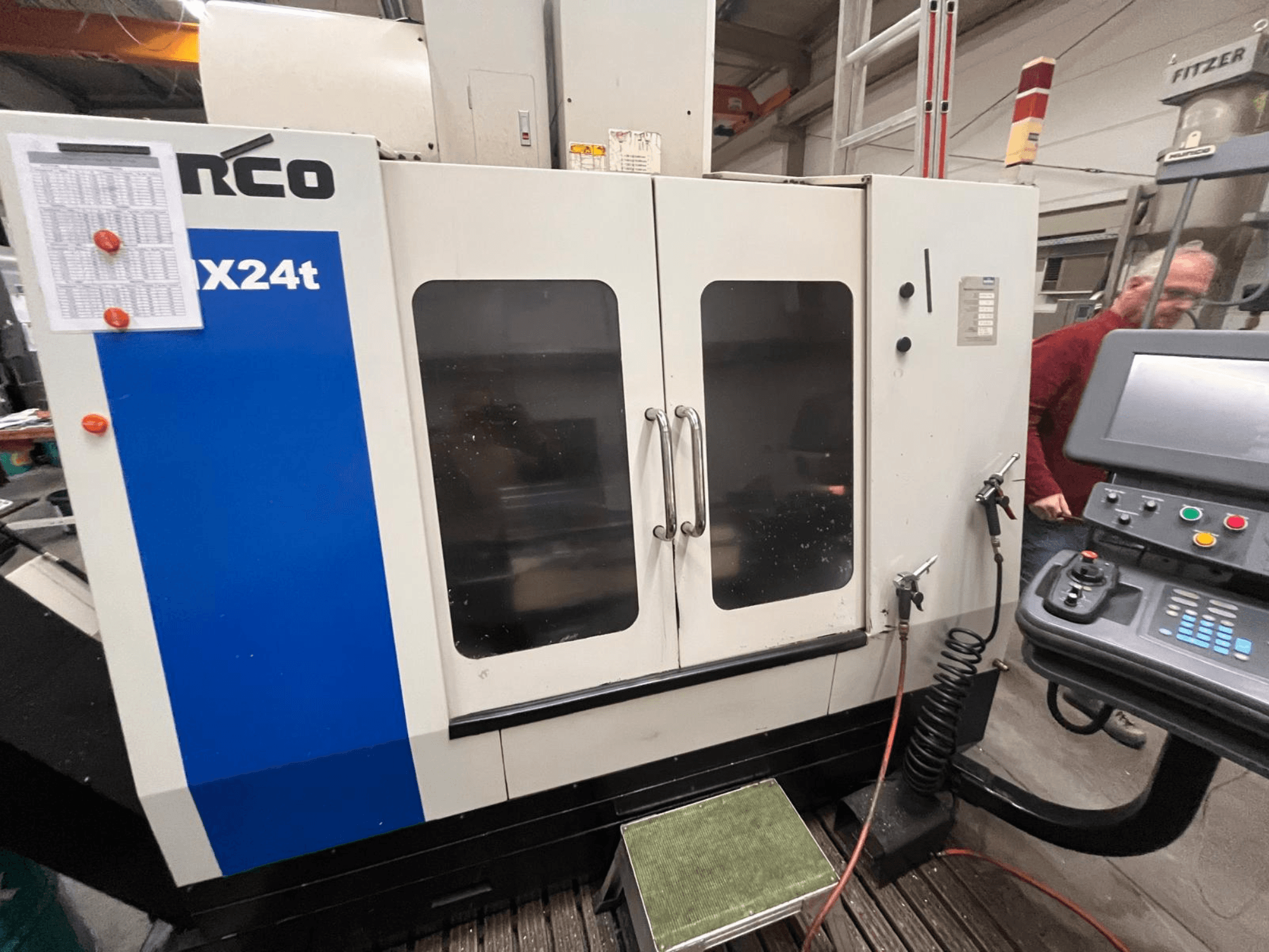 Вертикальный обрабатывающий центр Hurco, модель VX24t, показан спереди с панелью управления и прозрачными дверцами.