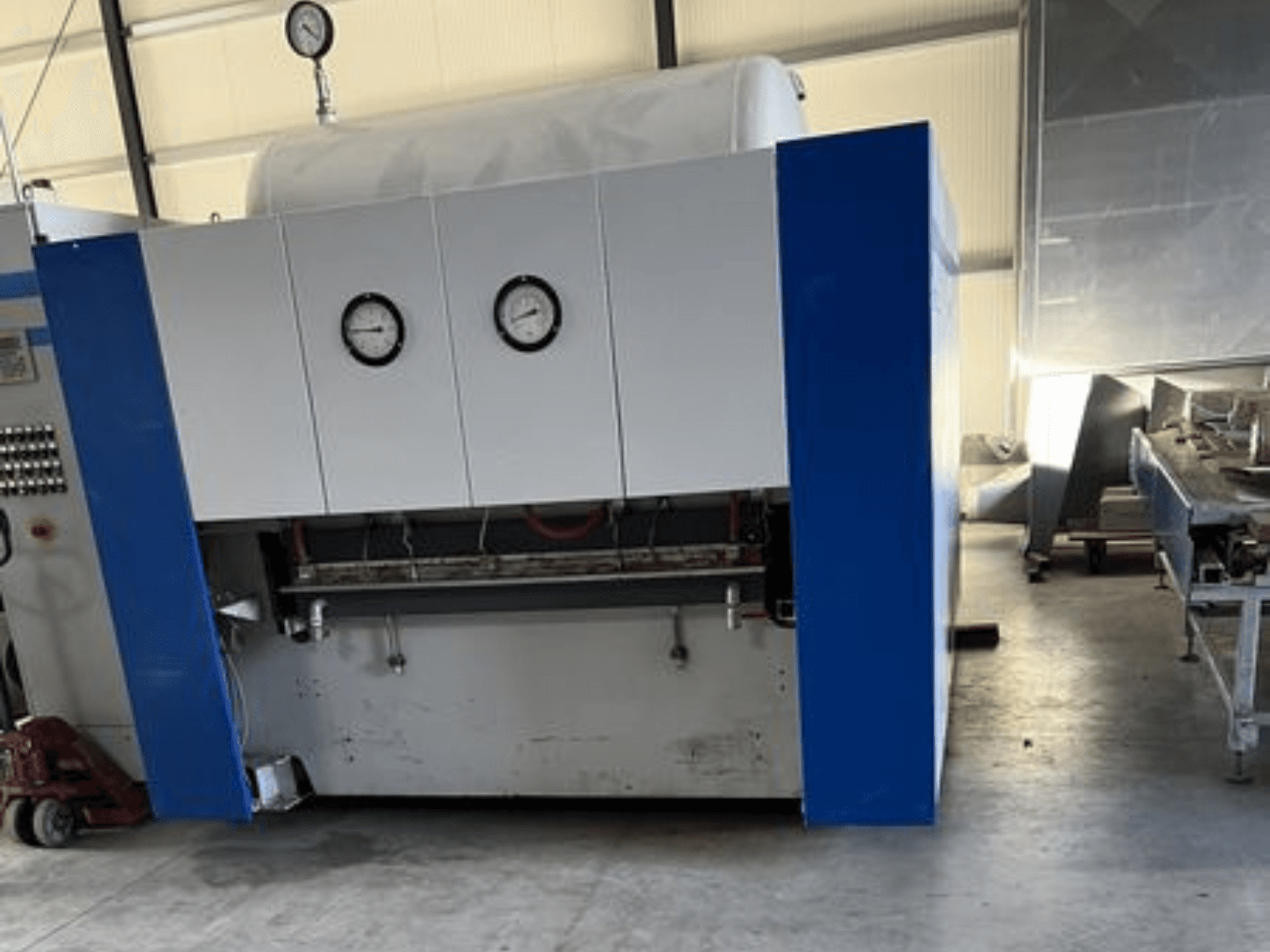 Сине-белый промышленный станок с двумя манометрами, вид спереди, с панелью управления и соседним оборудованием.