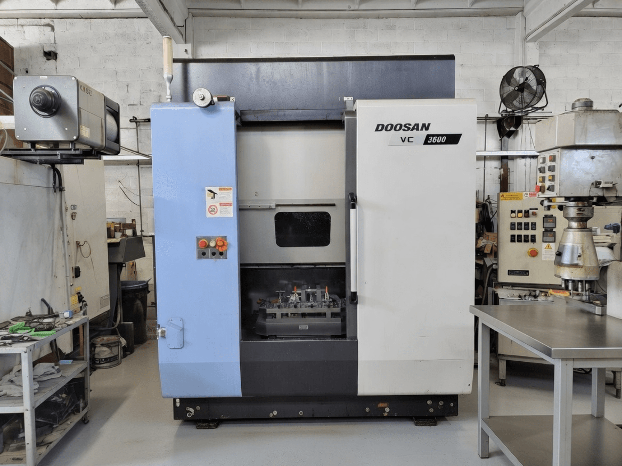 Вертикальный обрабатывающий центр DOOSAN VC 3600 (вид спереди), панель управления и открытая дверь, открывающая рабочую зону.