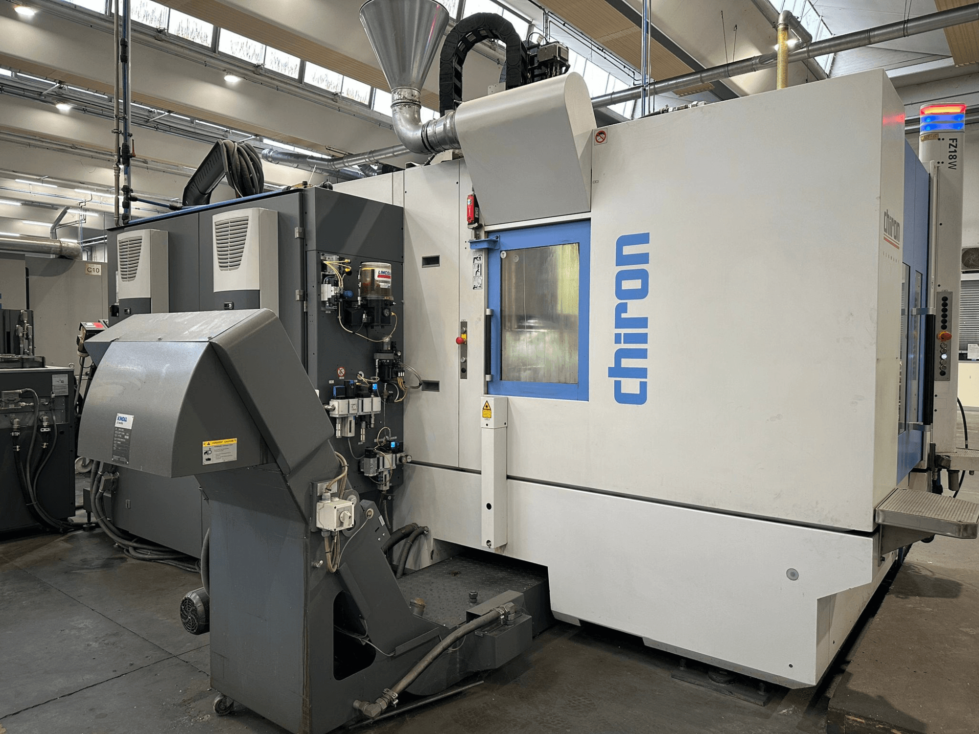 Станок с ЧПУ Chiron в серо-белом цвете, вид спереди, с элементами управления, трубами и кожухом для удаления пыли.