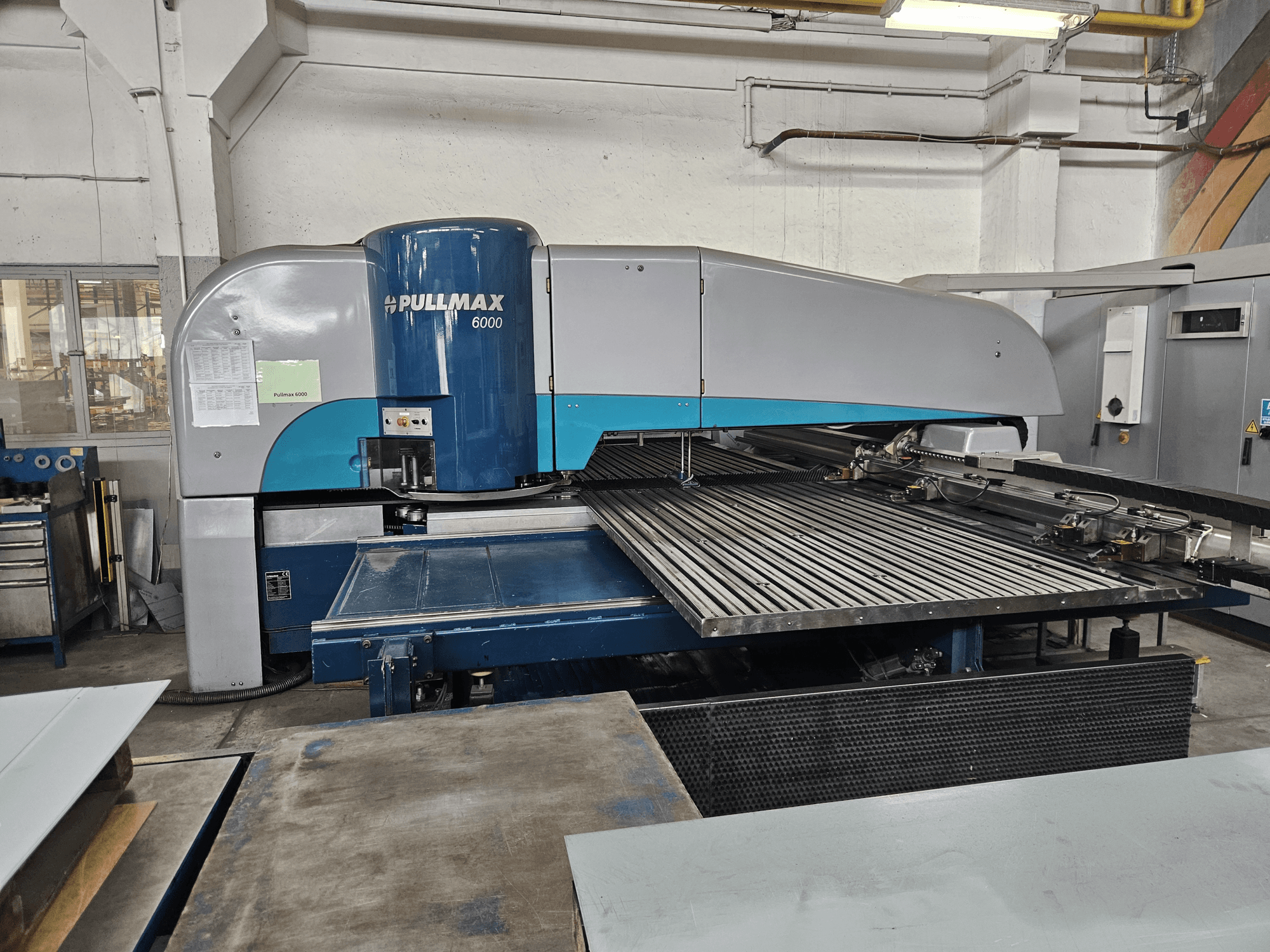 Вид спереди на пробивной станок с ЧПУ Pullmax 6000, демонстрирующий его большую планшайбу и металлический каркас в условиях мастерской.
