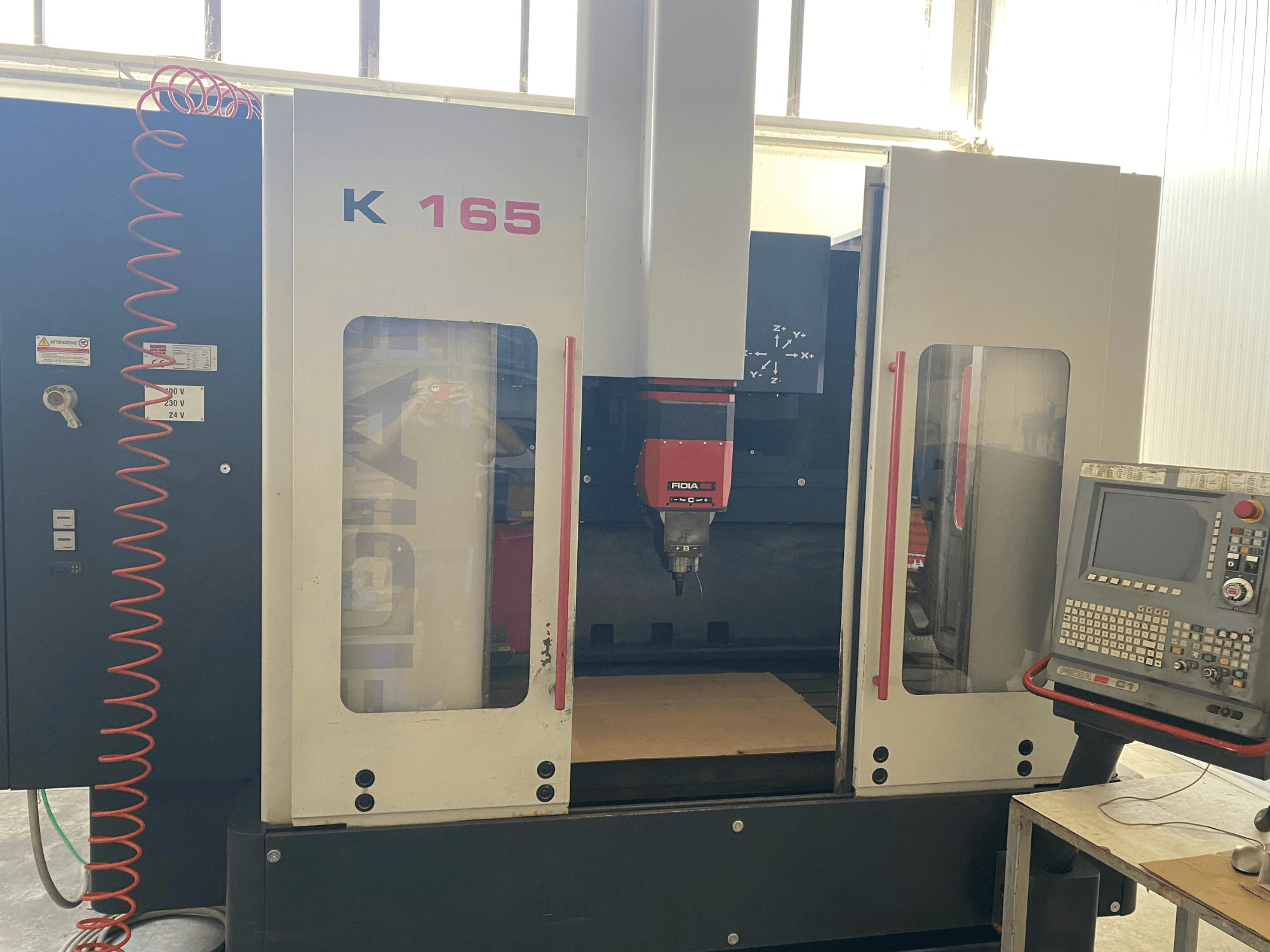 Станок с ЧПУ Fidia K 165 с красным шпинделем и панелью управления, вид спереди, в хорошо освещенной мастерской.