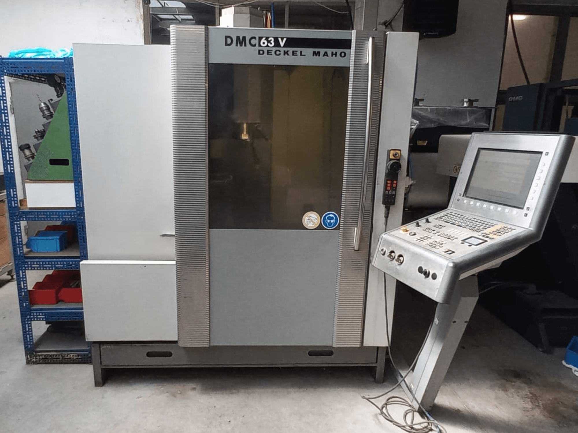 Вид спереди на вертикальный обрабатывающий центр DMG DECKEL MAHO DMC 63V с панелью управления и видимой рабочей зоной.