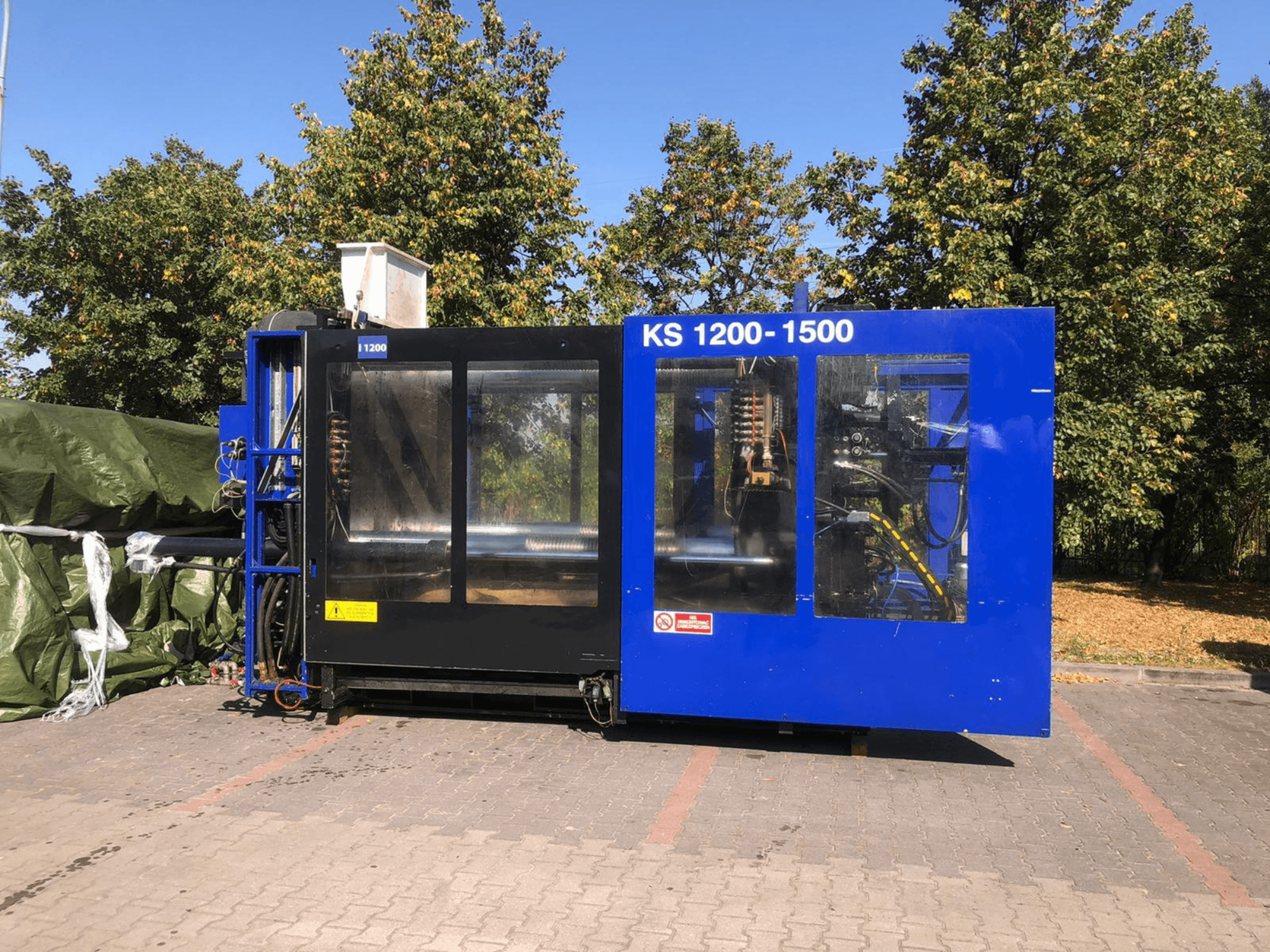 Гидравлическая машина для литья под давлением ITALTECH KS 1200 8300 ES, вид сбоку, демонстрирующая органы управления и детали оборудования в парковой обстановке.