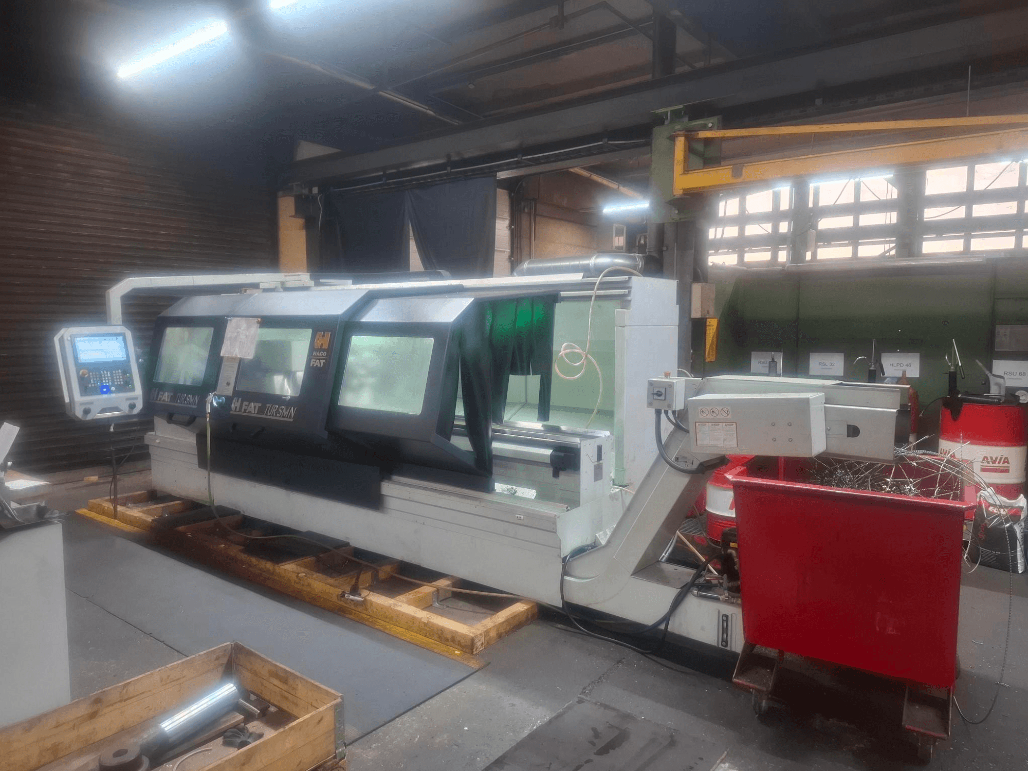 Вид спереди на станок с ЧПУ FAT Tursan с панелью управления, установленный на деревянных поддонах в цеху.