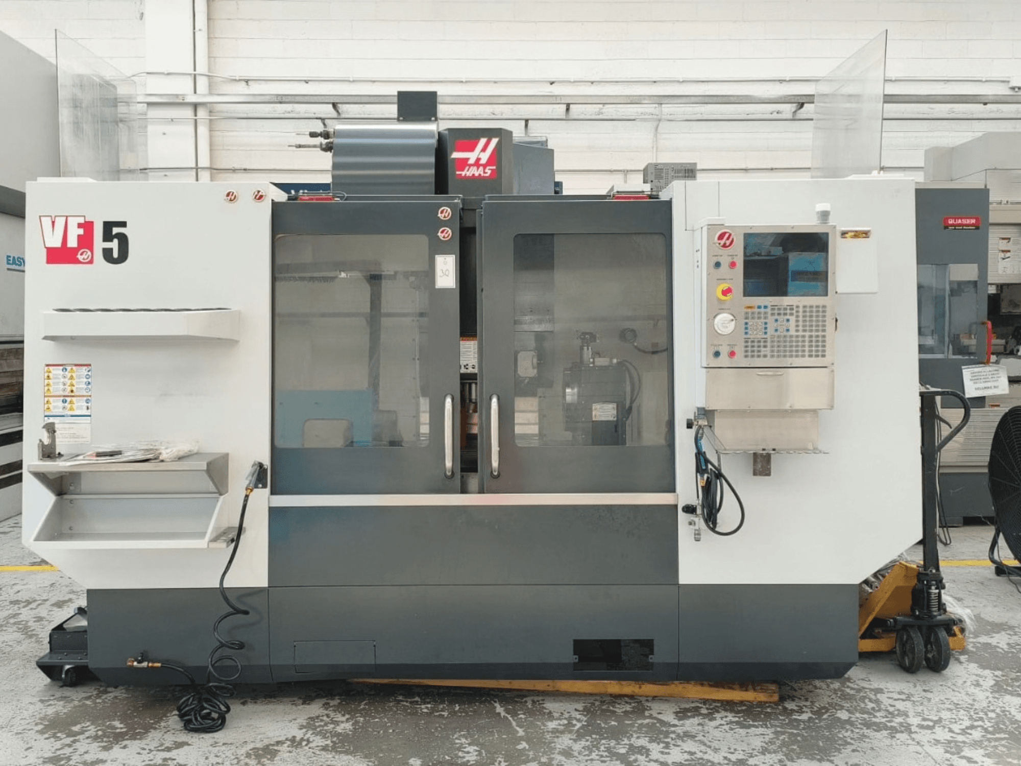 Вертикальный обрабатывающий центр HAAS VF 5/40, вид спереди, с панелью управления и стеклянными дверцами.