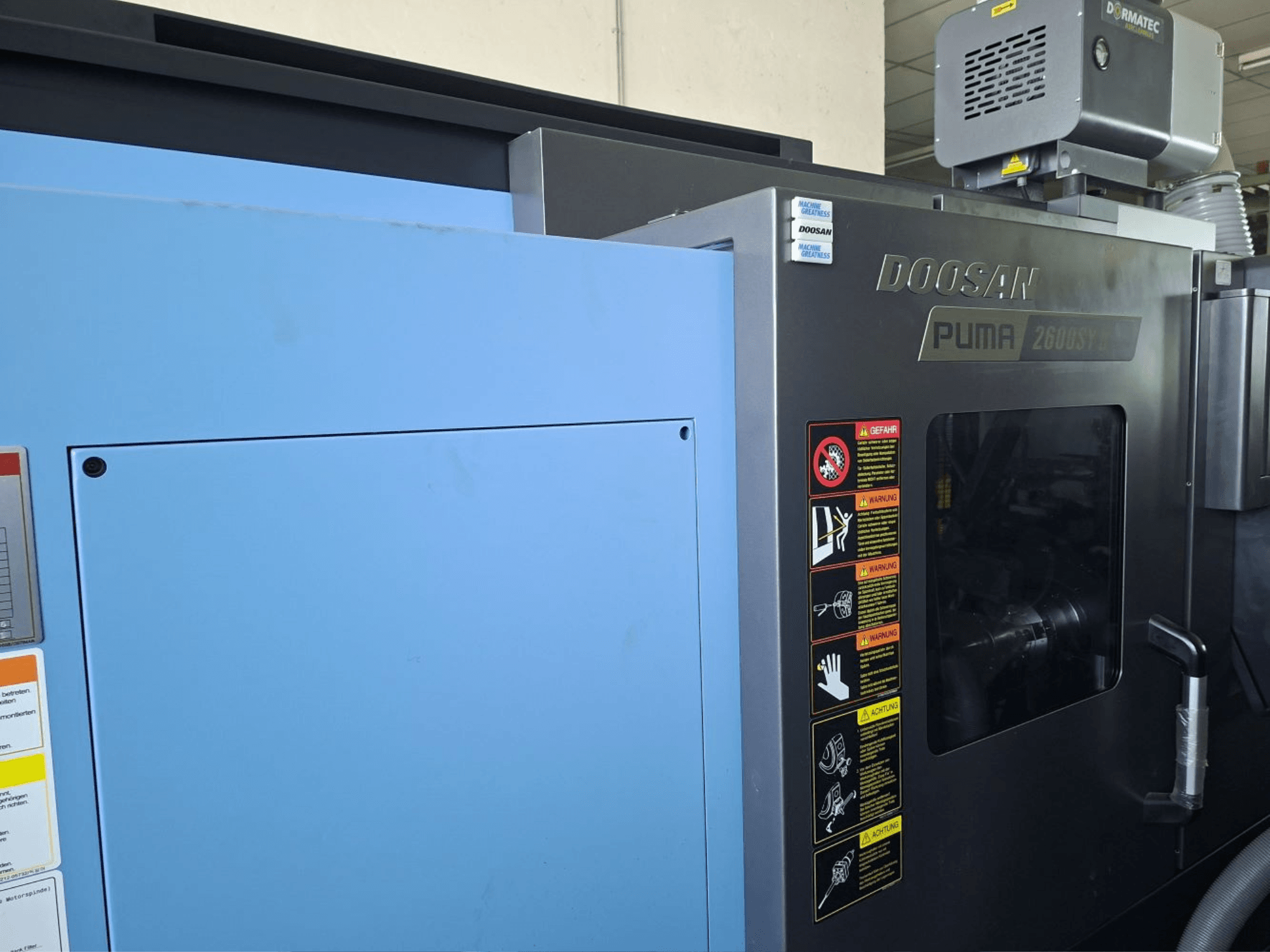 Горизонтальный токарный станок DOOSAN PUMA 2600 SY II, вид спереди, демонстрирует защитные наклейки и синюю обшивку.
