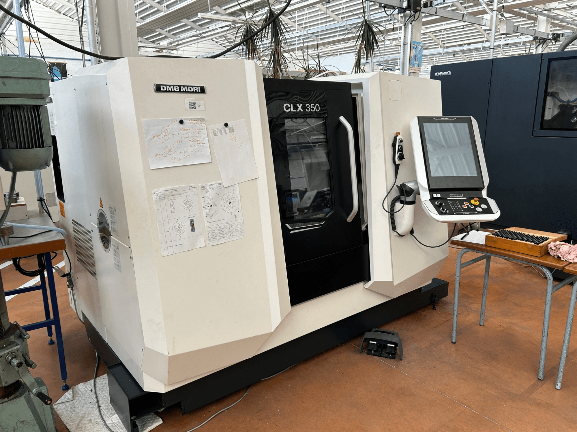 Горизонтальный токарный станок DMG MORI CLX 350 V4, вид спереди с панелью управления и прилагаемой технической документацией.