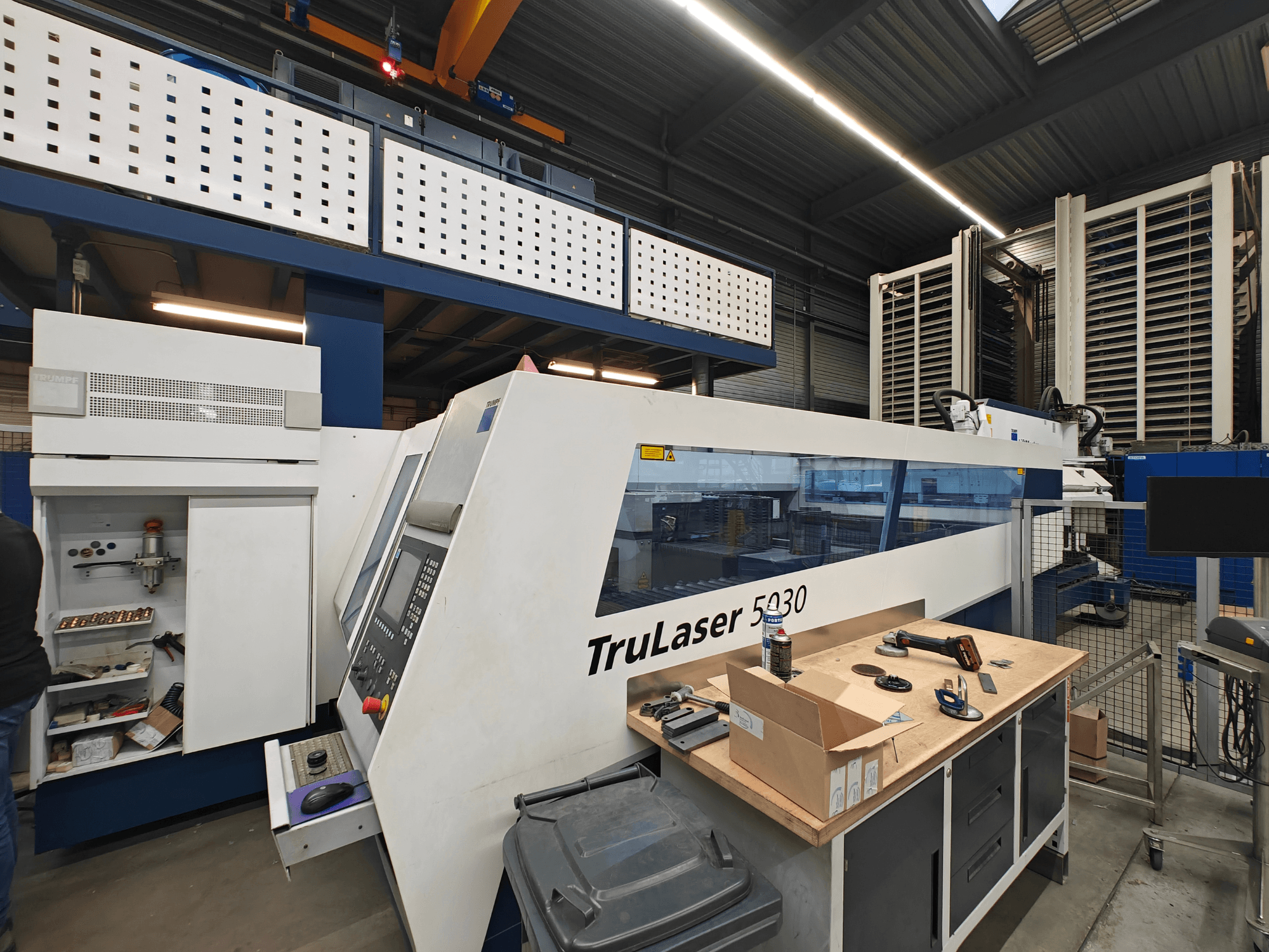 Станок TruLaser 5030 в мастерской, вид спереди, видна панель управления, в окружении инструментов и оборудования.
