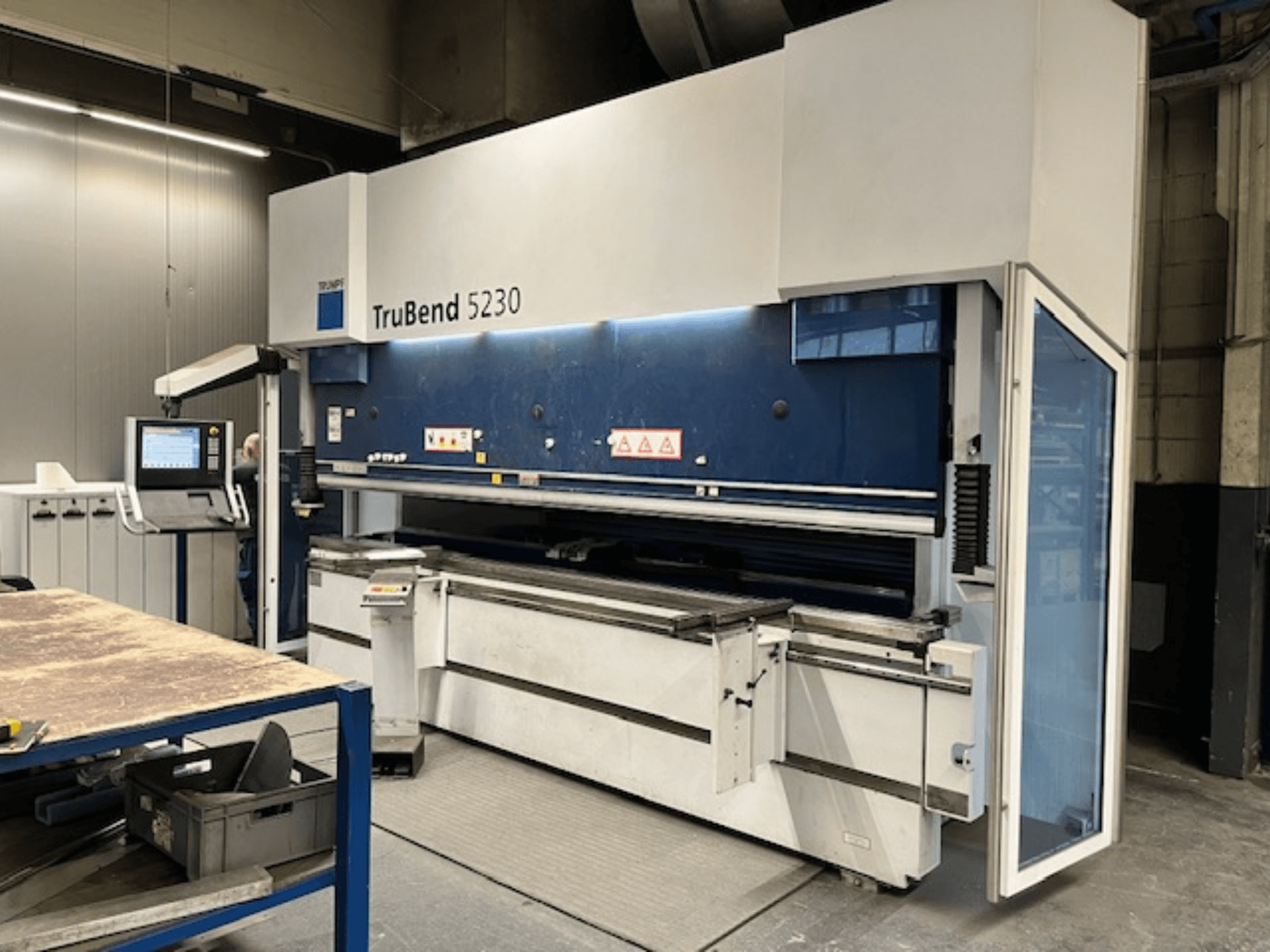 Гибочный станок TruBend 5230 в промышленных условиях; вид спереди, показывающий панель управления, элементы безопасности и рабочий стол.