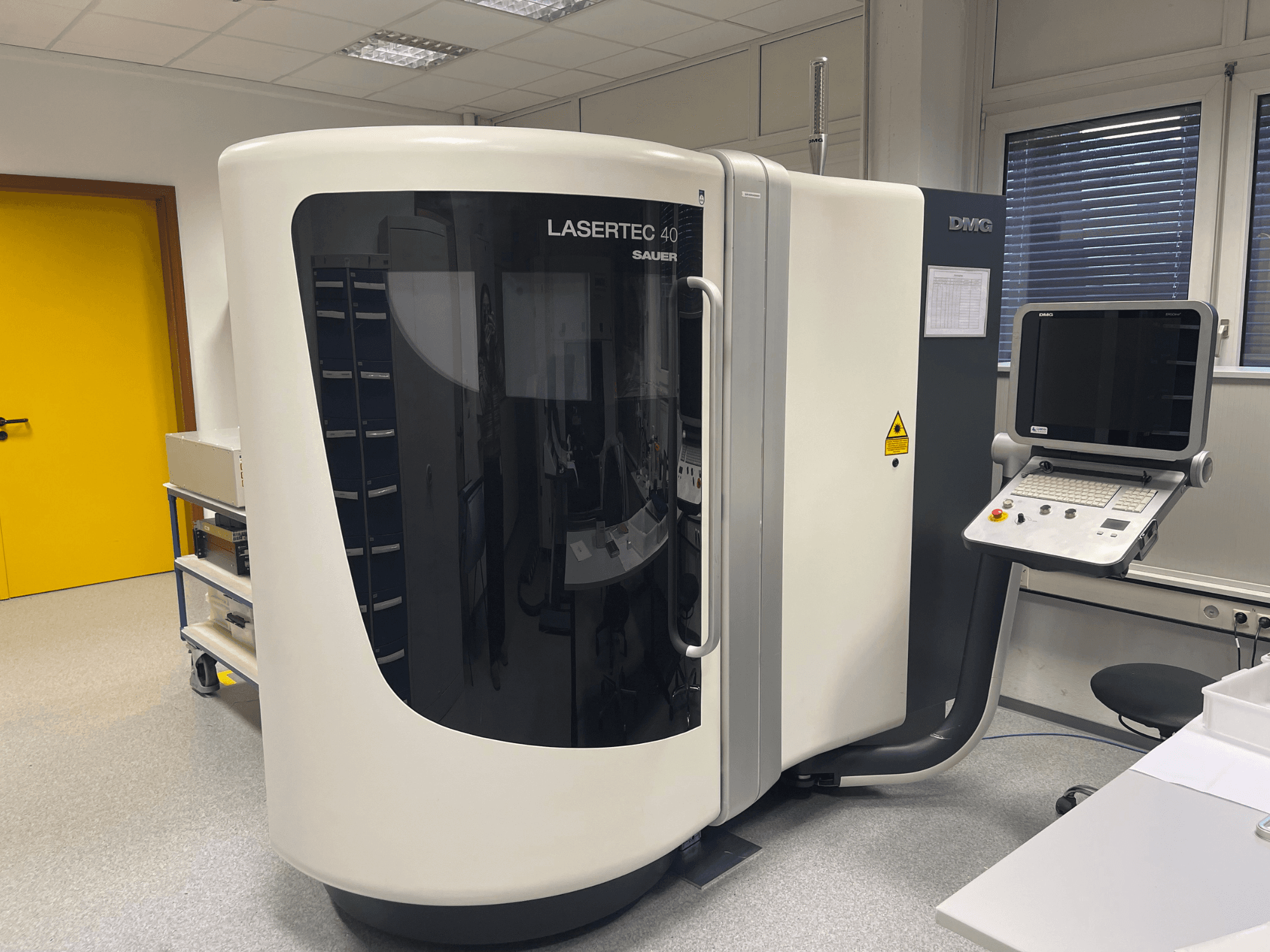 Белый фрезерный станок LASERTEC 40 производства DMG MORI, вид спереди, панель управления и эргономичный дизайн в хорошо освещенном помещении.