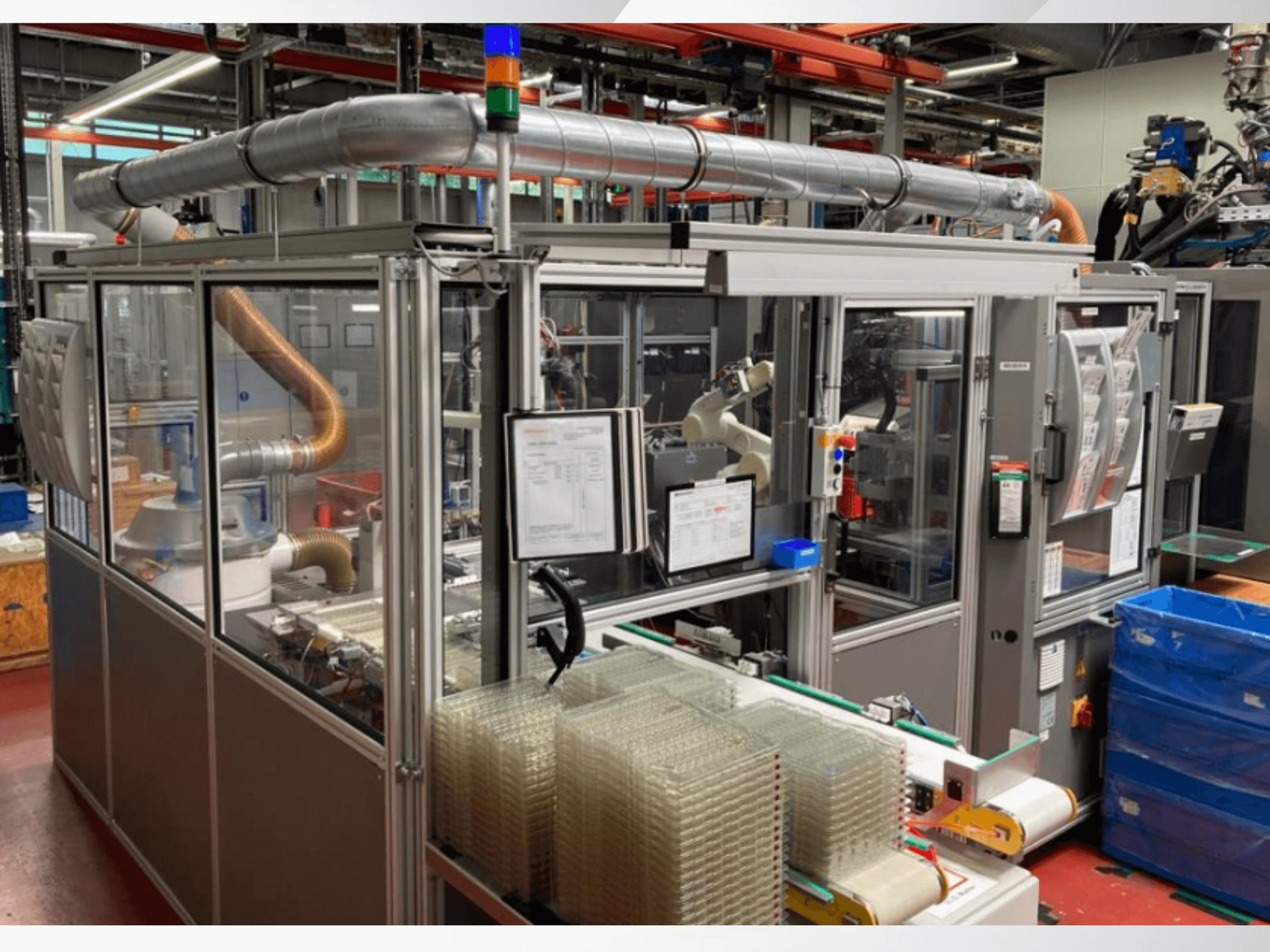 Автоматическая сборочная машина с роботизированной рукой, прозрачными боковыми панелями и штабелями контейнеров с прозрачными предметами, вид спереди.