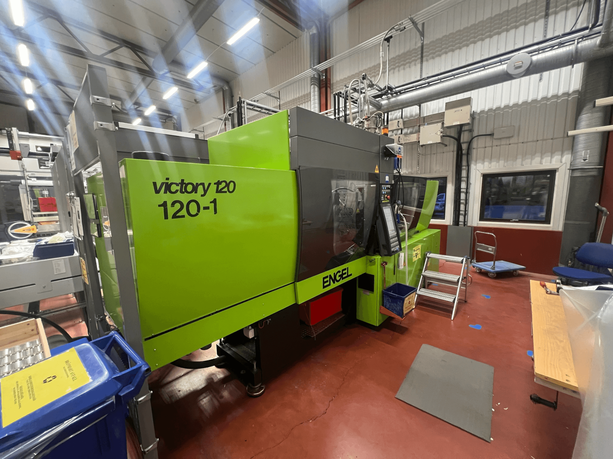 Зеленый термопластавтомат ENGEL Victory 120-1, вид спереди, с панелью управления и ступенями, в промышленной обстановке.