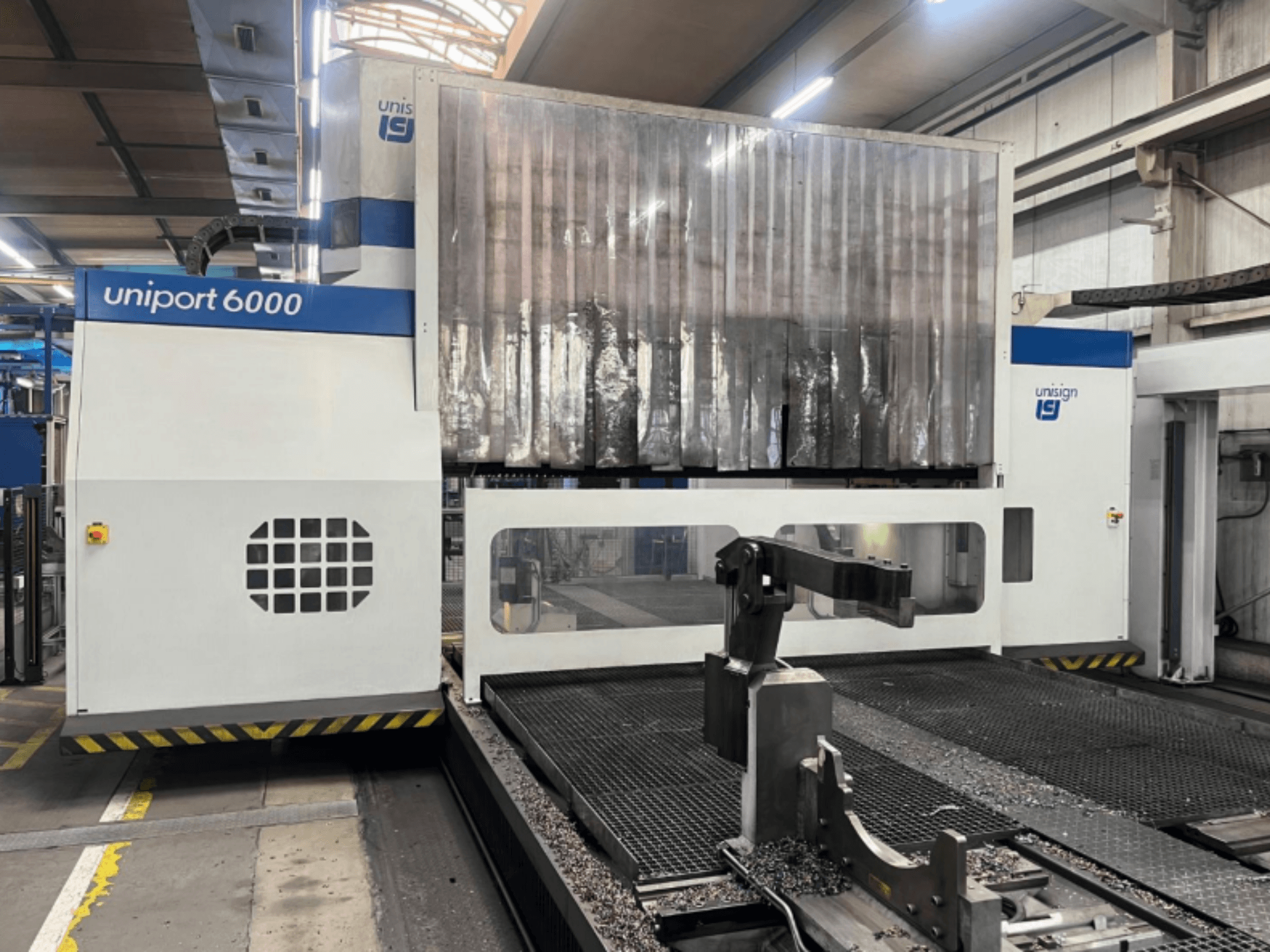 Портальный фрезерный станок Unisign uniport 6000, вид спереди, демонстрирующий конструкцию станка и зону резки с металлической стружкой.
