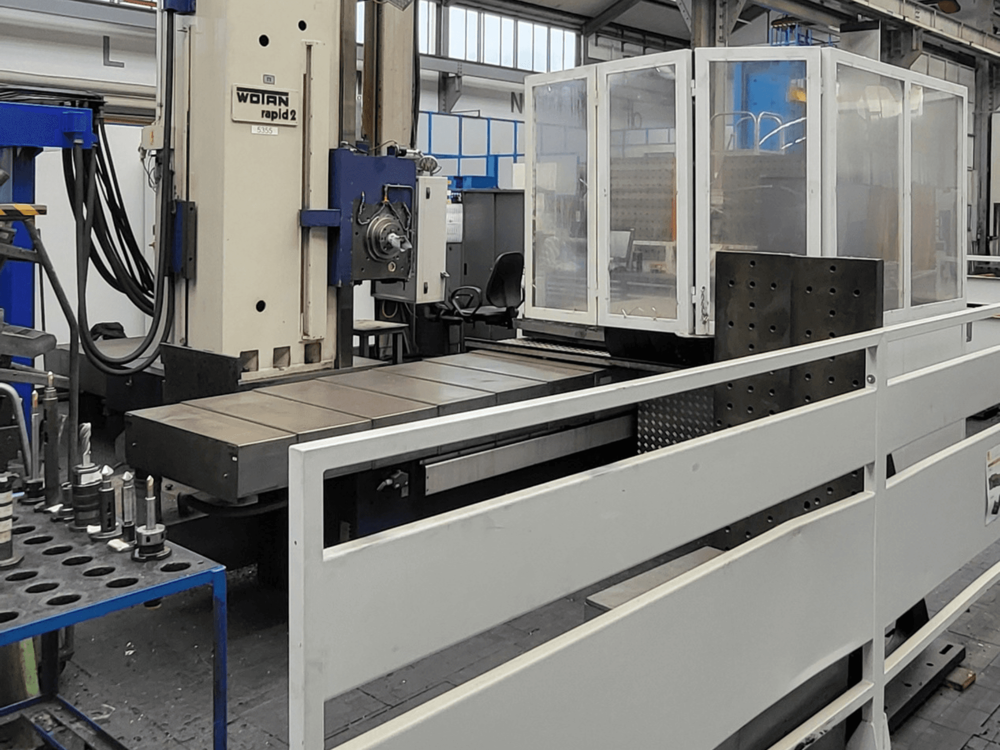 Горизонтальный обрабатывающий центр WOTAN Rapid 2R/6-1500/2, изображенный в виде спереди, с большим рабочим столом и защитным кожухом.