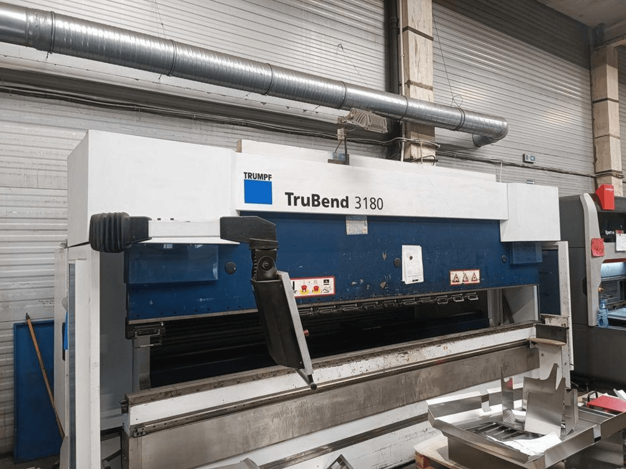 Гибочный станок Trumpf TruBend 3180 в мастерской, вид сбоку на панель управления и металлические детали на столе.