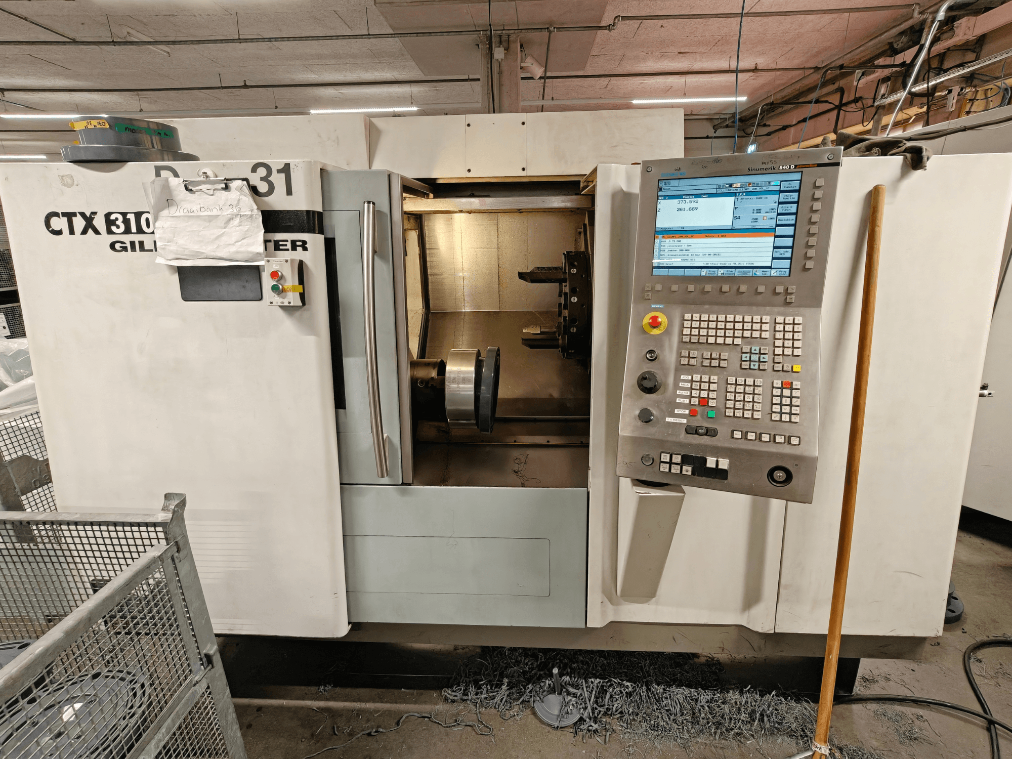 Горизонтальный токарный станок Gildemeister CTX 310, вид спереди с панелью управления, с указанием инструментов и рабочего пространства внутри.