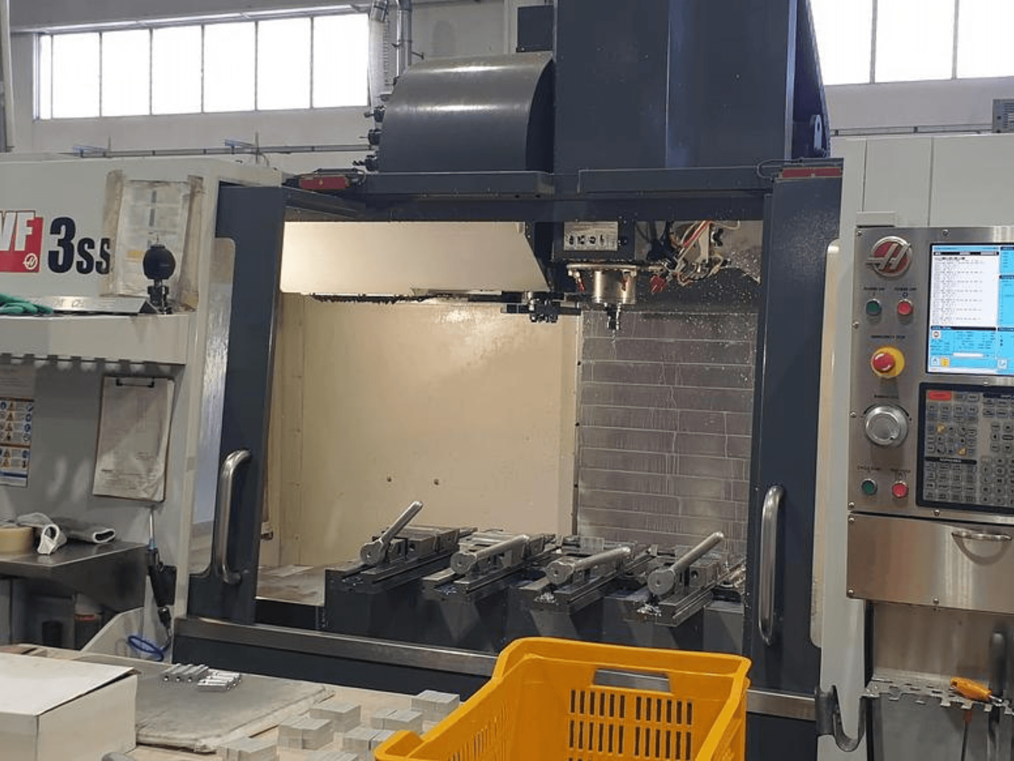 Вертикальный обрабатывающий центр HAAS VF-3SS, вид спереди с панелью управления ЧПУ, инструментами и оранжевой корзиной.