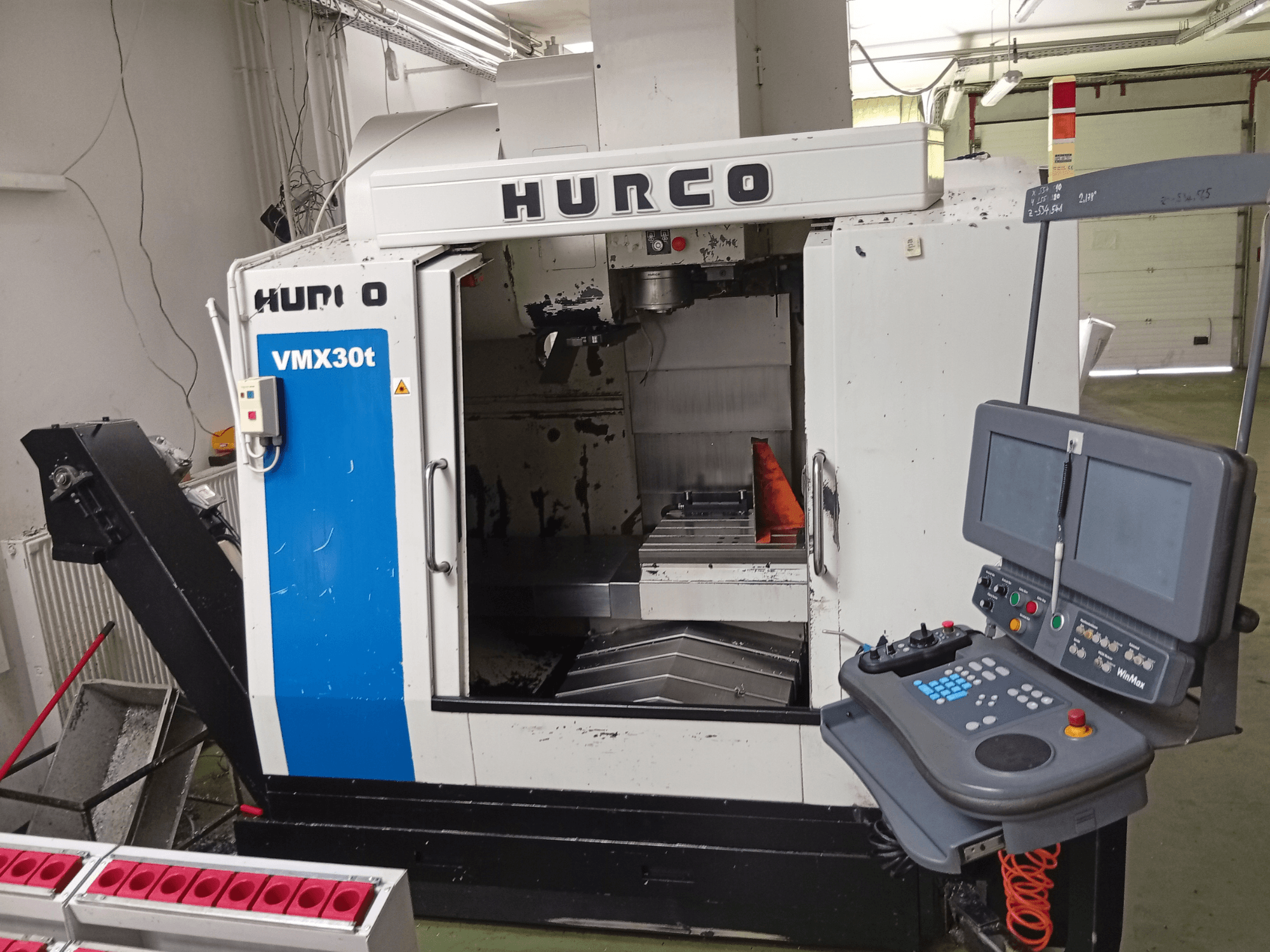 Вертикальный обрабатывающий центр Hurco VMX 30T, вид спереди, с панелью управления и зоной шпинделя, на фоне которого виден рабочий стол.