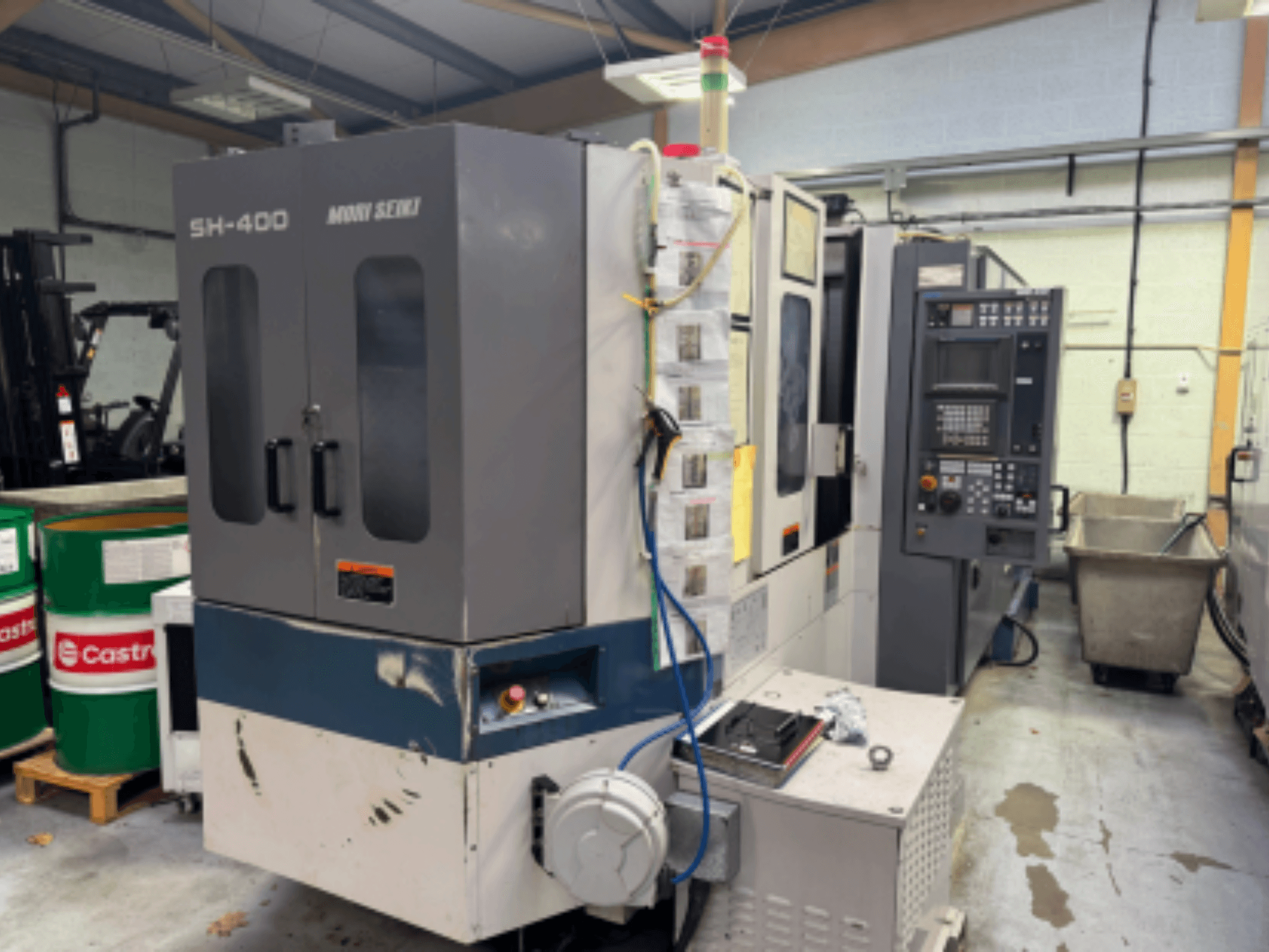 Станок с ЧПУ Moni Seiki SH-400, вид сбоку с изображением панели управления, дверей и окружающей промышленной обстановки.