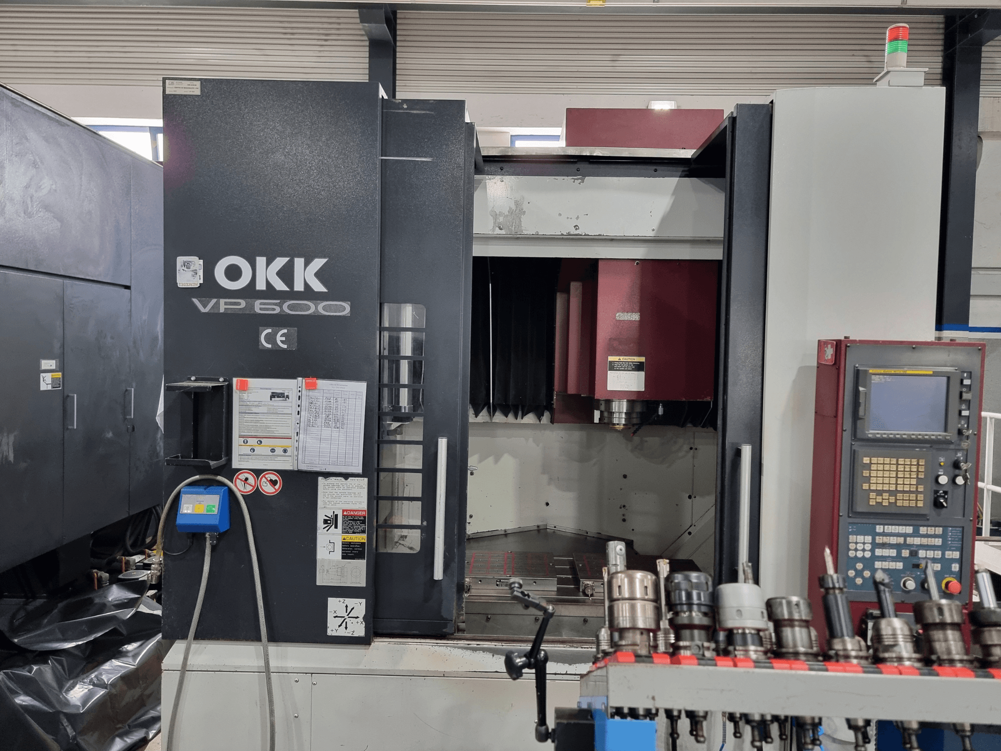 Вертикальный обрабатывающий центр OKK VP600, вид спереди, на котором видны панель управления и держатели инструментов, установленные на стойке.