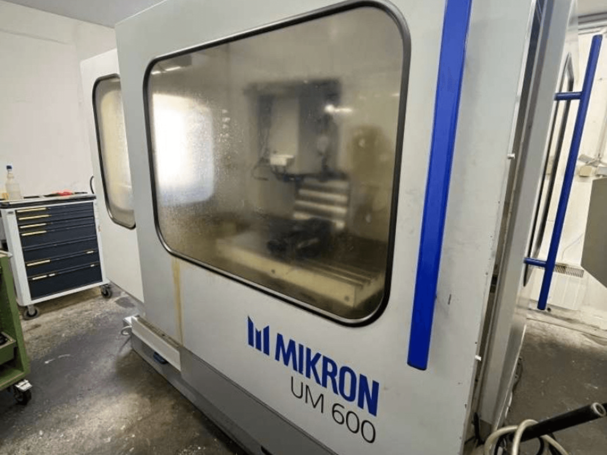 Универсальный обрабатывающий центр MIKRON UM 600 TNC 410/426, вид сбоку, с запотевшим стеклом и видимым рядом хранилищем инструментов.