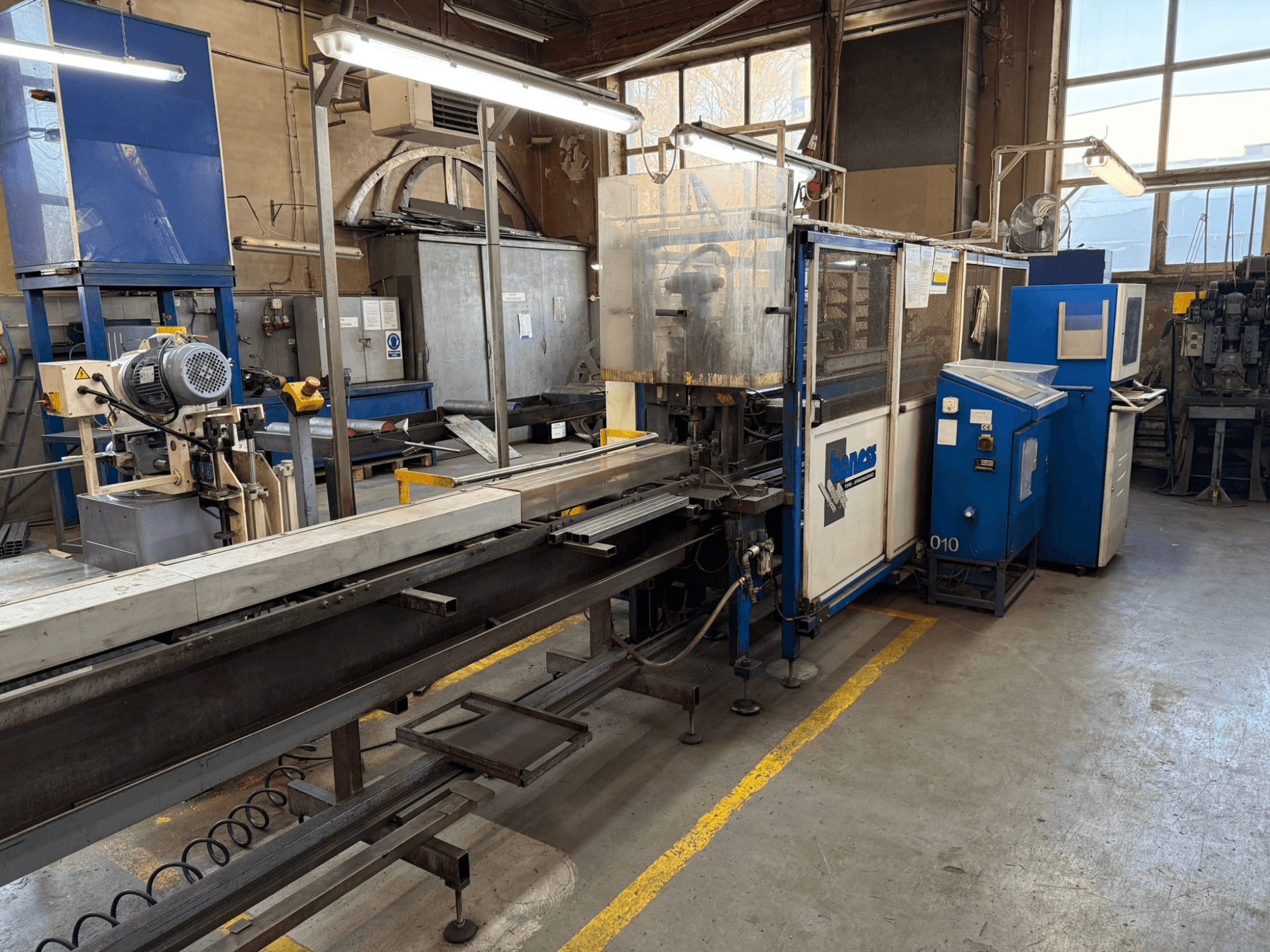 Промышленная мастерская с синим станком Haweas, вид сбоку с изображением конвейера и оборудования в большом, хорошо освещенном помещении.