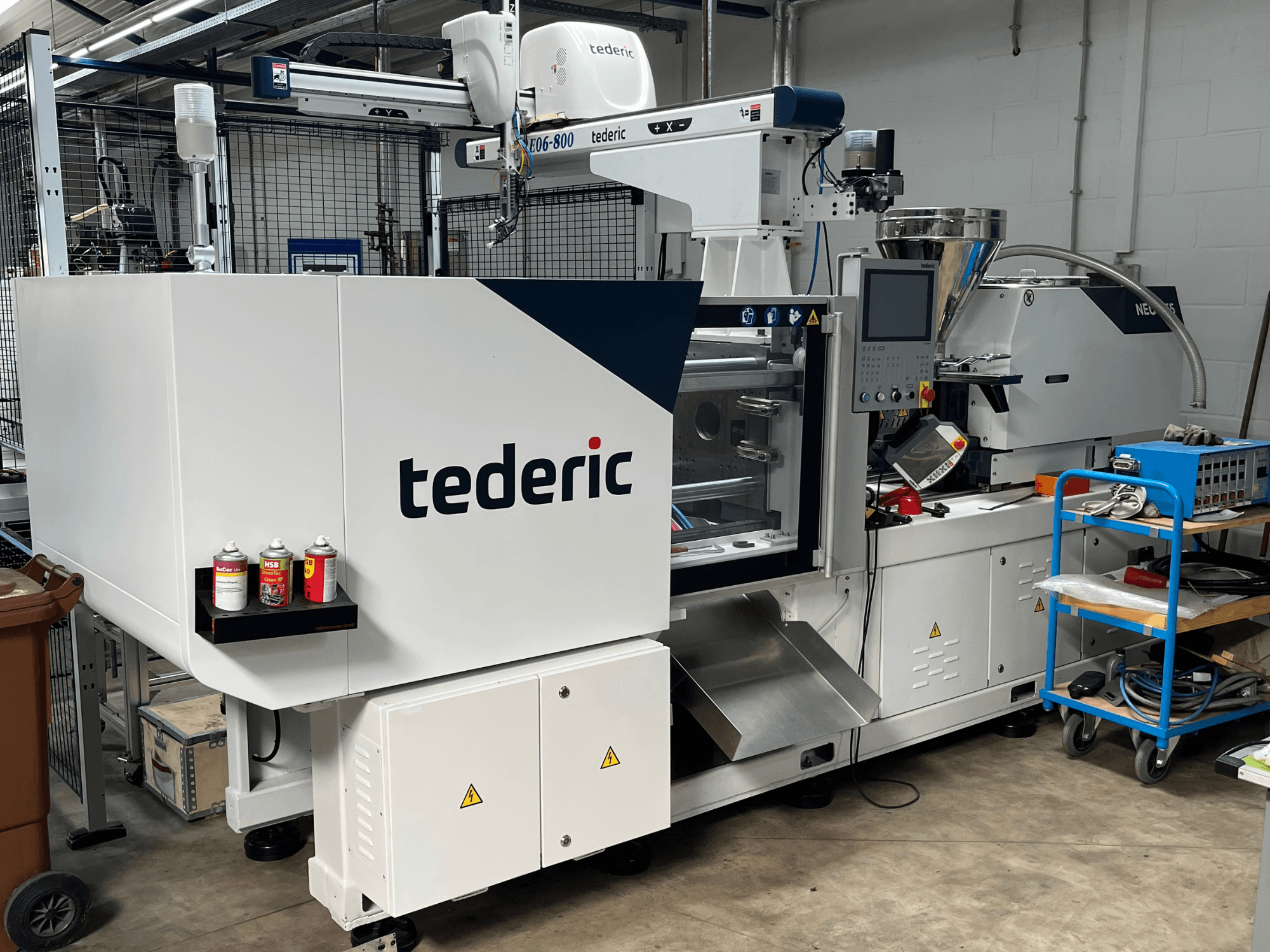 Гидравлическая термопластавтомат TEDERIC NEO.E55/e110h в цехе, вид сбоку с панелью управления и расположенными рядом инструментами.