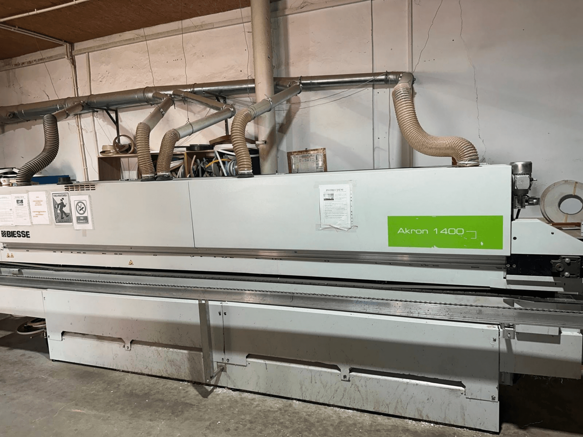 Кромкооблицовочная машина BIESSE Akron 1440 A в виде сбоку с видом на систему вытяжки, панель управления и наклейки с инструкциями по эксплуатации.