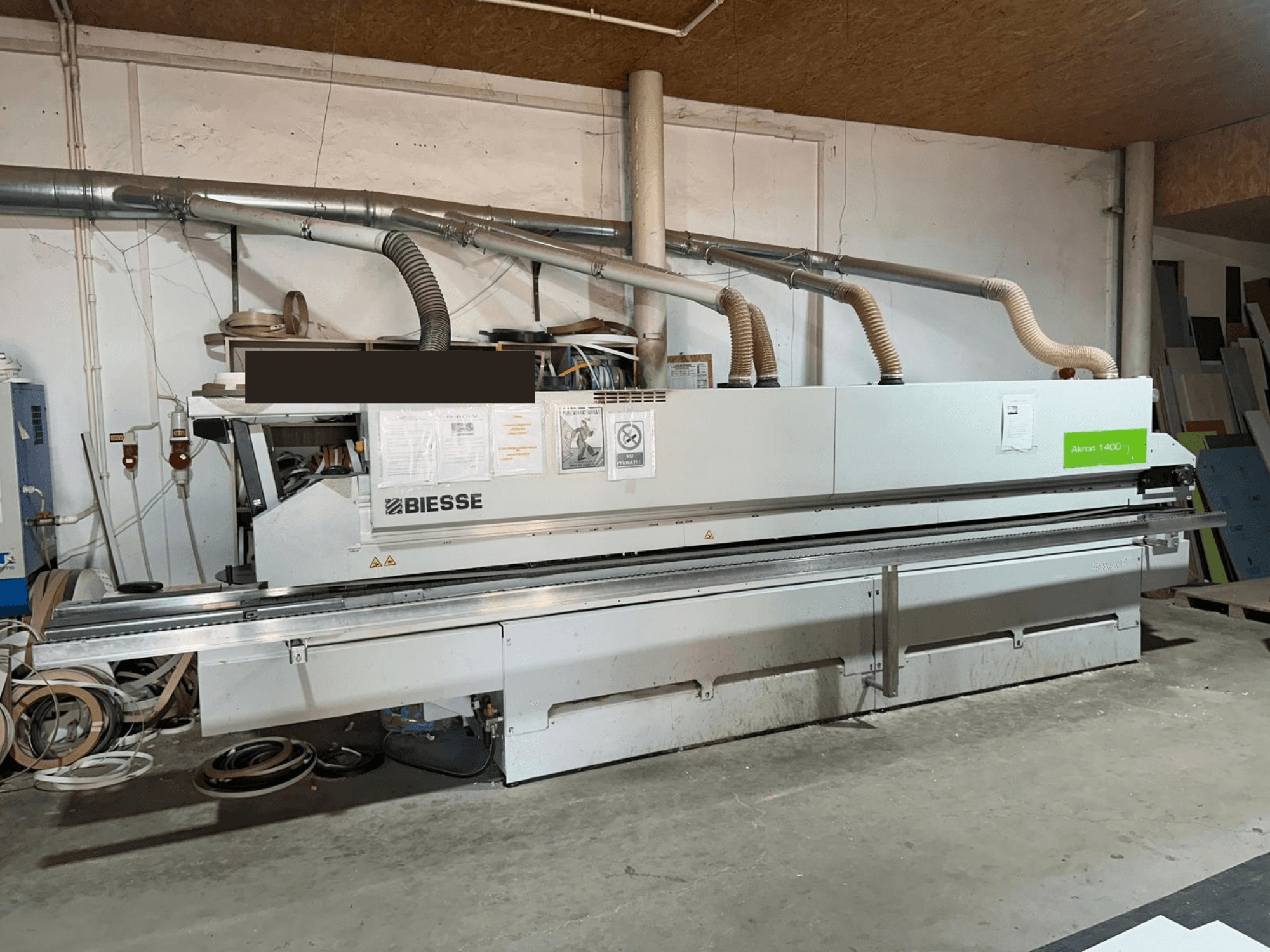 Кромкооблицовочная машина BIESSE AKRON 1440 A, вид спереди, с хорошо заметной панелью управления и элементами системы пылеудаления в условиях цеха.