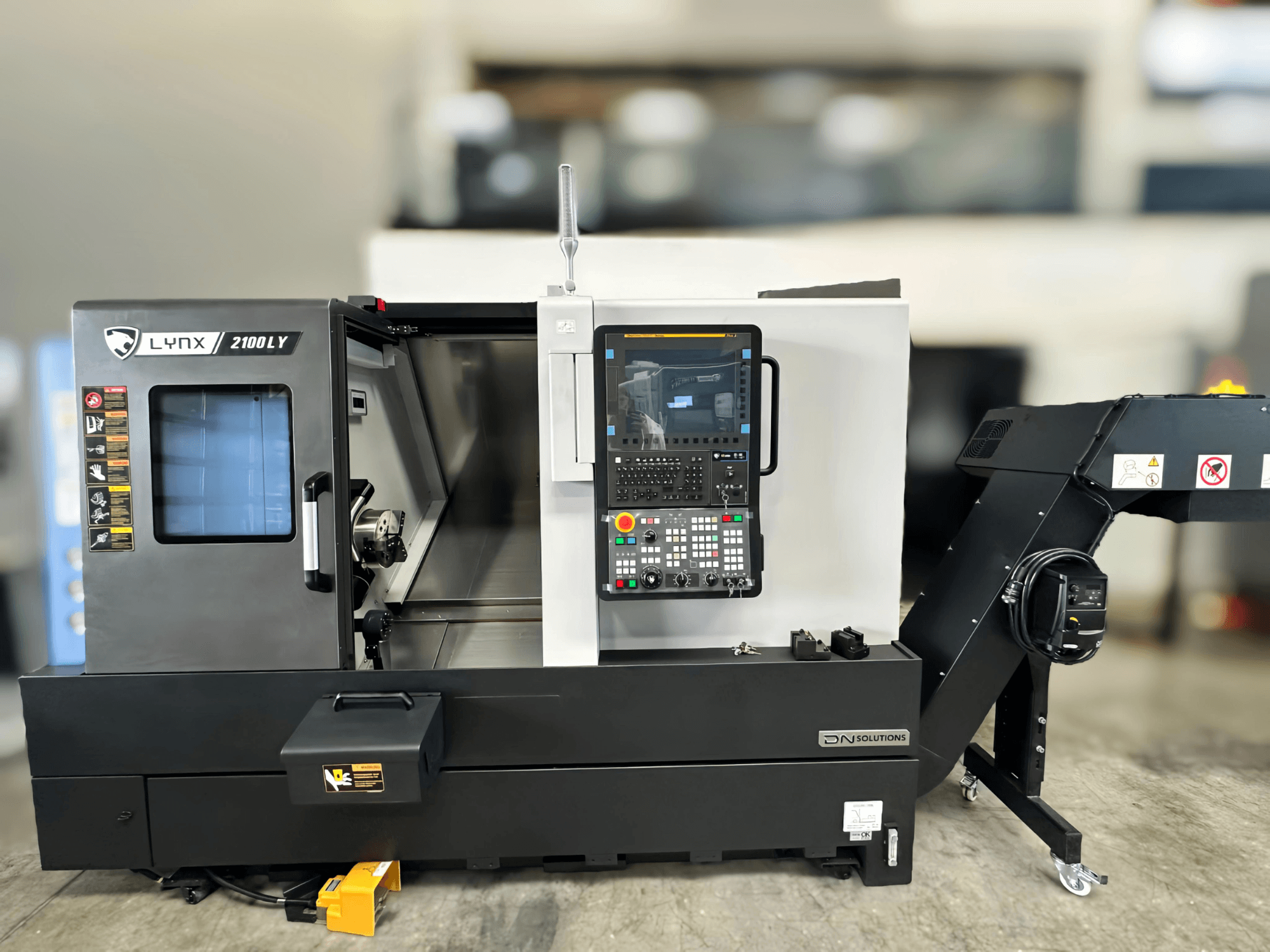 Горизонтальный токарный станок DN SOLUTIONS LYNX 2100LYB, вид спереди, с панелью управления и открытой дверью, открывающей внутреннее пространство.