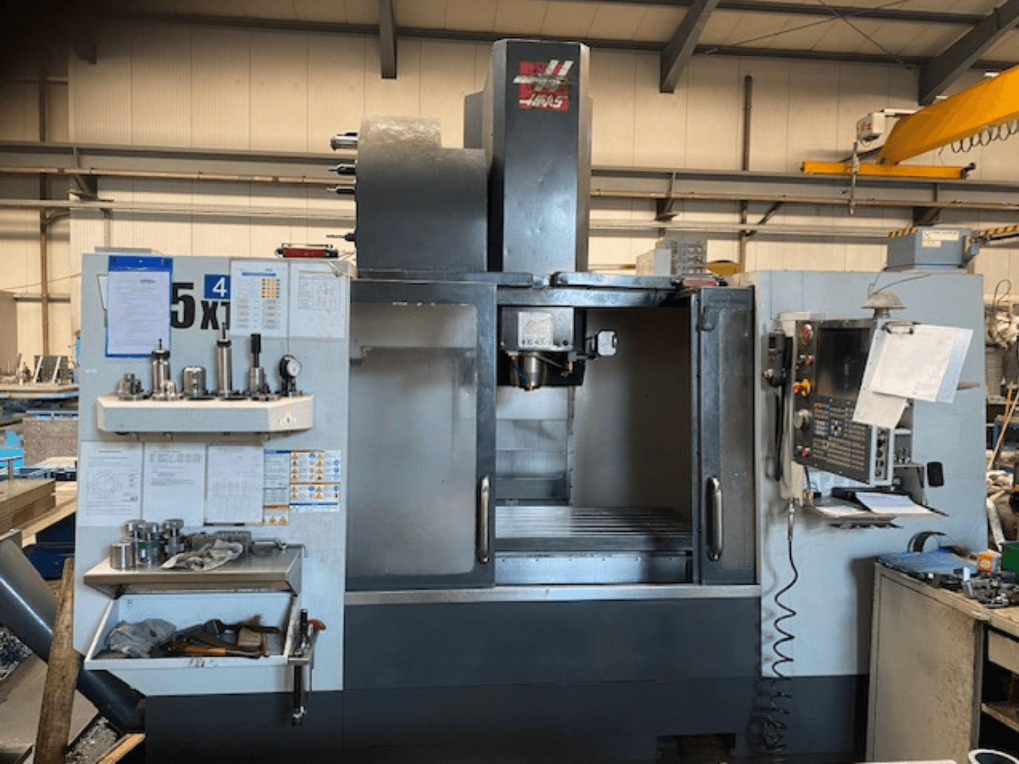 Вертикальный обрабатывающий центр Haas VF-5, вид спереди, демонстрирует панель управления, хранилище инструментов и область шпинделя.