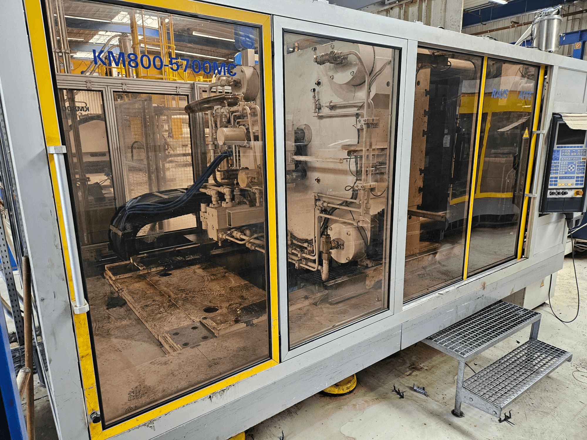 Гидравлическая термопластавтомат Krauss Maffei KM800-5700 MC, вид спереди, демонстрирующий компоненты через стеклянные панели.