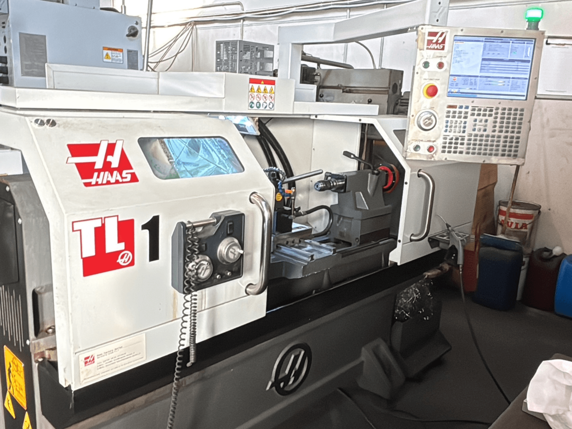 Токарный станок с ЧПУ Haas TL-1, вид спереди, панель управления с дисплеем, держатель инструмента и наклейки безопасности.