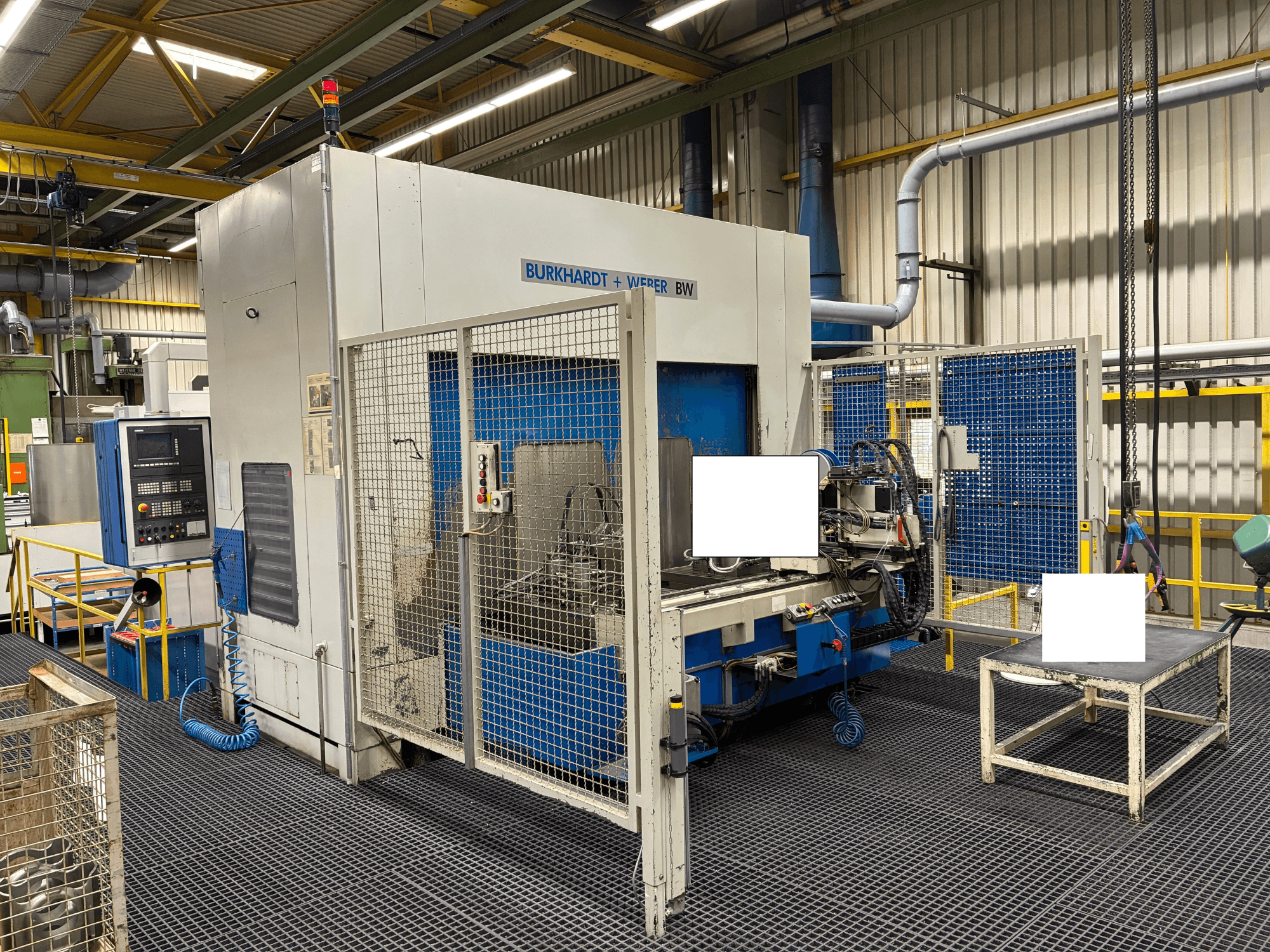 Обрабатывающий центр Burkhardt + Weber BW, вид спереди, панель управления и защитный кожух, расположен в промышленном помещении.