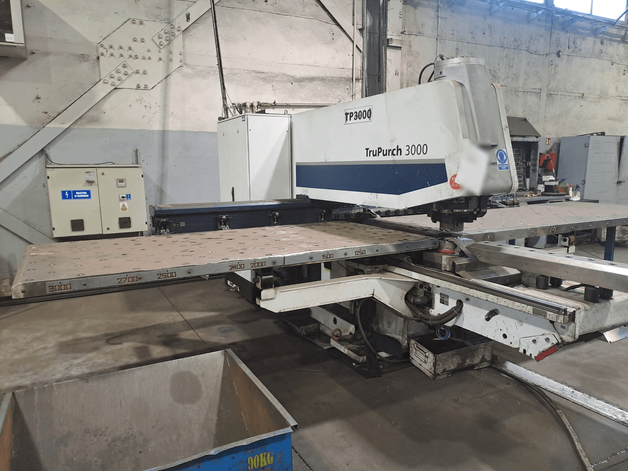 Станок с ЧПУ TruPunch 3000 показан спереди, с большой металлической пластиной и измерительными метками, в промышленных условиях.