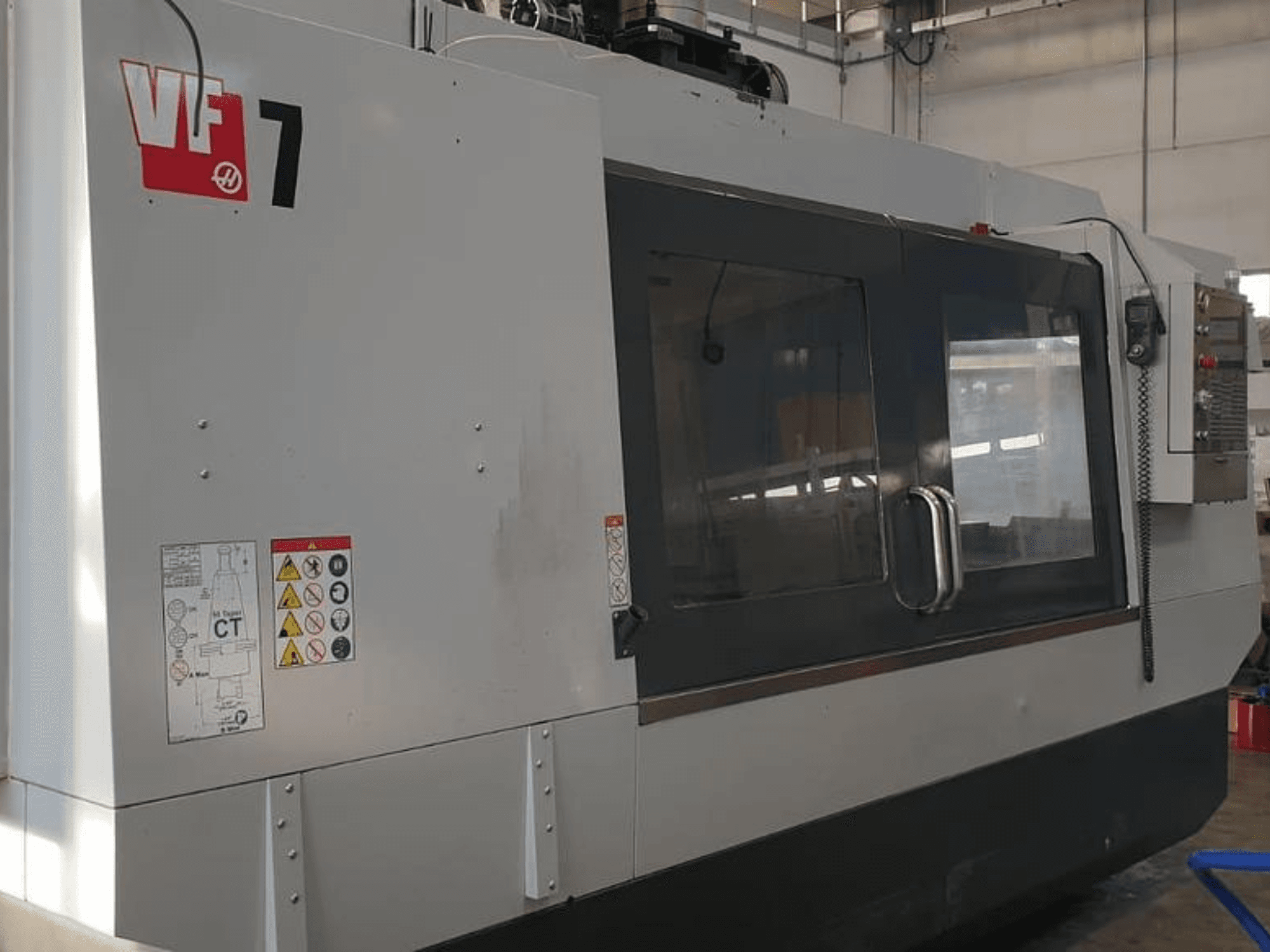 Станок с ЧПУ Haas VF-7 с видом сбоку, серая металлическая отделка, панель управления и наклейки безопасности.
