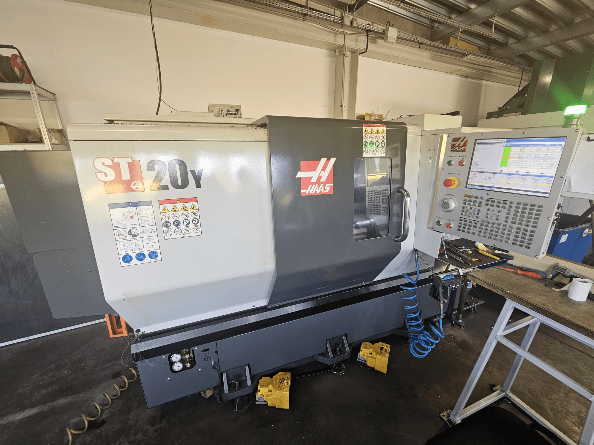Токарный станок с ЧПУ Haas ST-20Y спереди с панелью управления; наклейки безопасности и детали воздушного шланга сбоку.