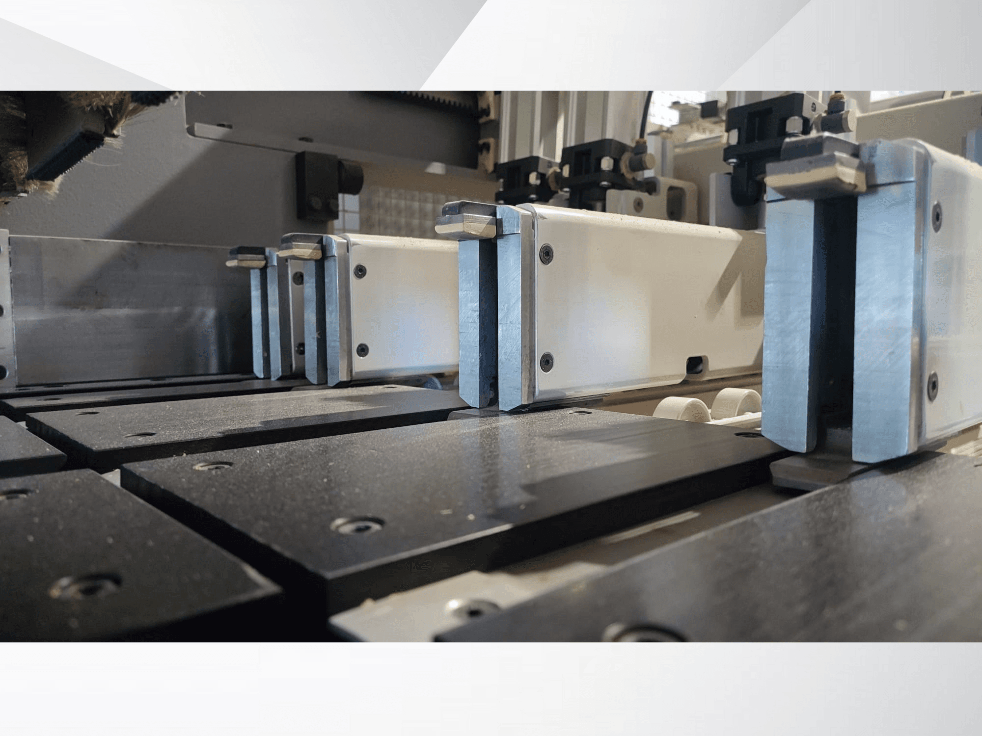 Крупный план зажимного механизма прецизионного станка с металлическими губками, с черными рабочими поверхностями и видимыми направляющими.