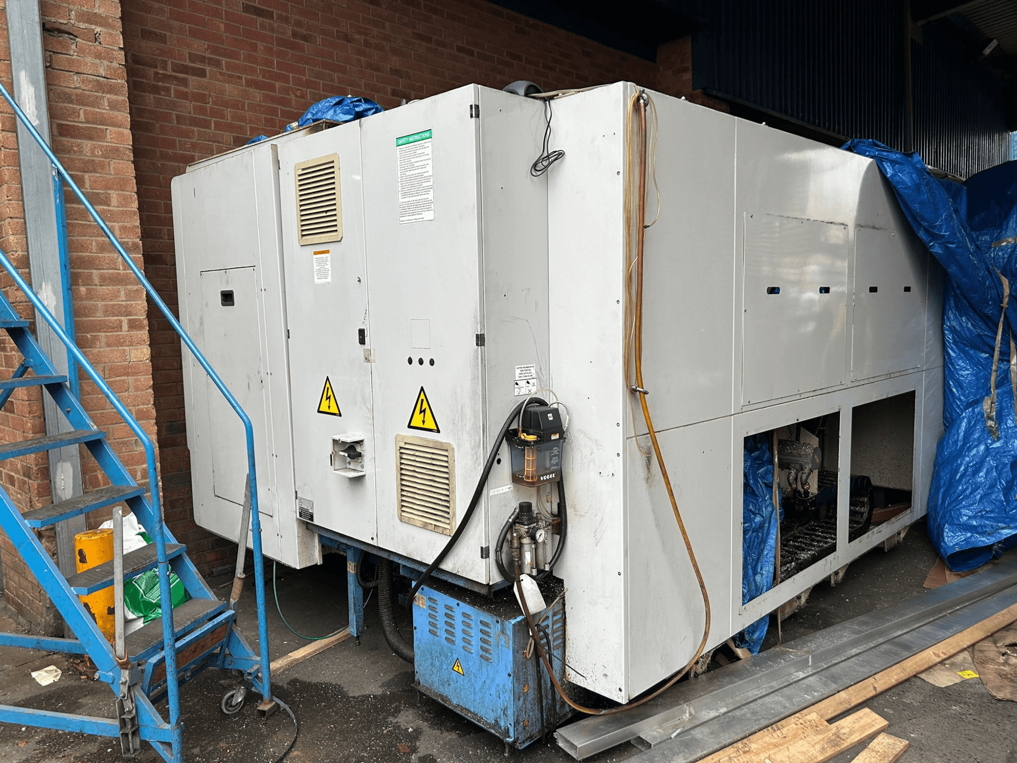 Вид сбоку большого промышленного холодильника, марка и модель не уточняются, с указанием электрических соединений, предупреждающих знаков и синего брезентового покрытия.