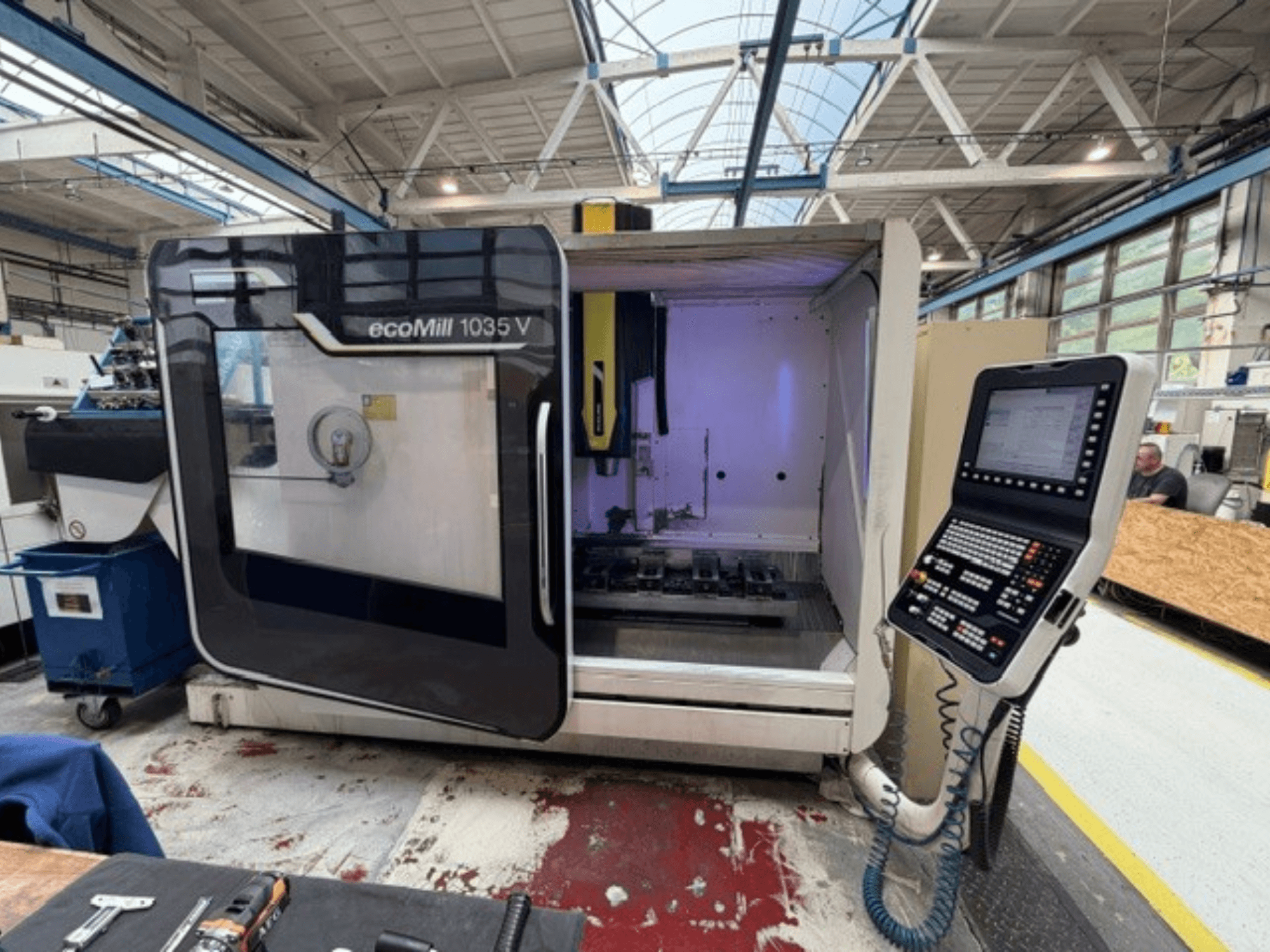 Вид спереди на вертикальный обрабатывающий центр DMG MORI ecoMill 1035V с открытой дверью, на котором видны панель управления и рабочая зона внутри.