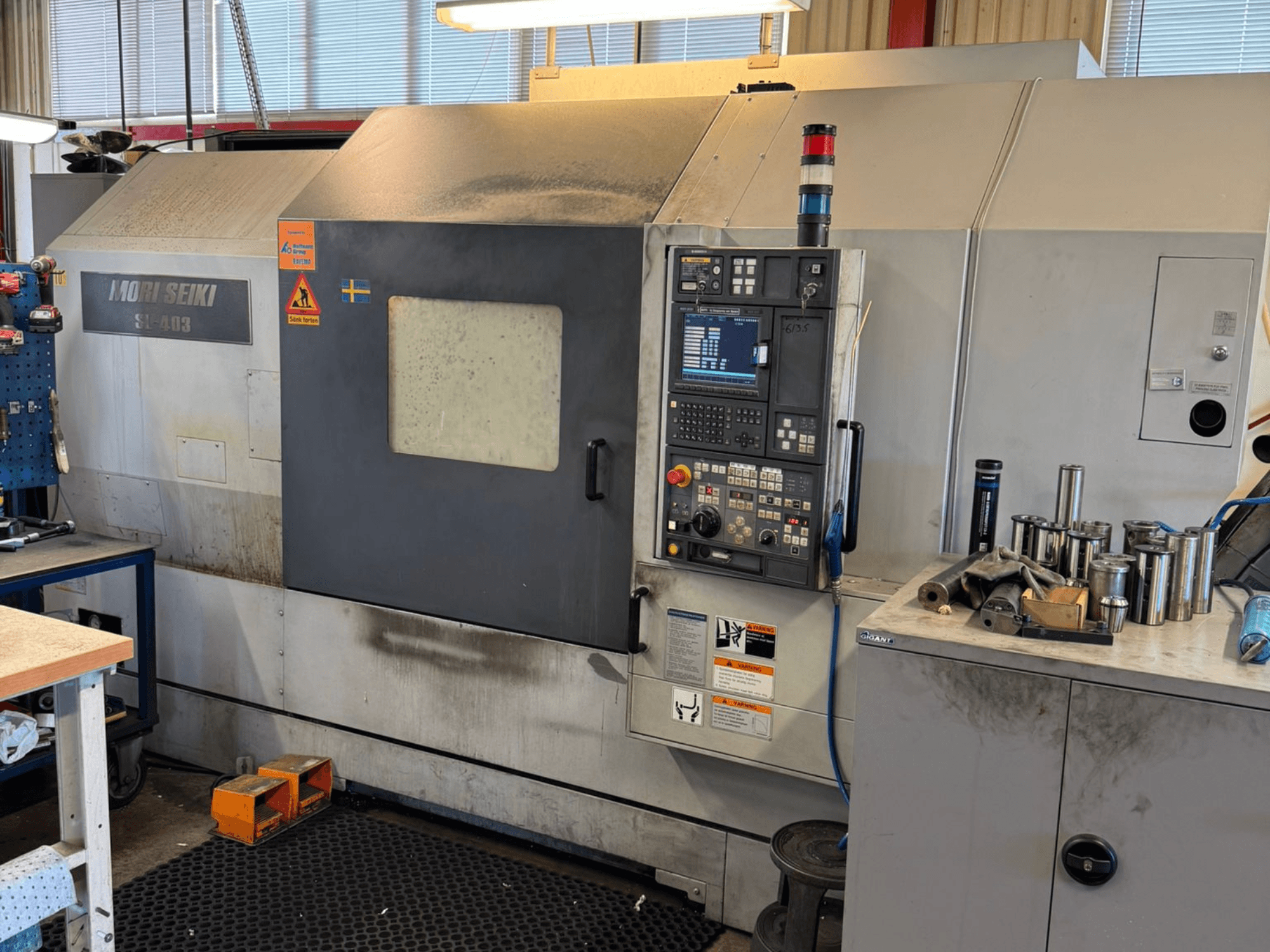 Горизонтальный токарный станок MORI SEIKI SL-403BMC/800 в мастерской, панель управления и близлежащие инструменты, вид сбоку.