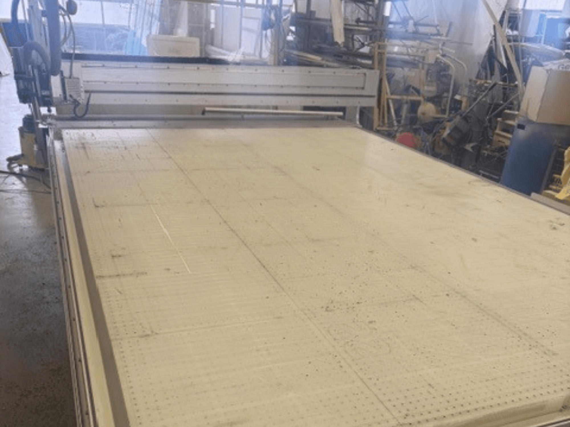 Большой отрезной станок с плоской поверхностью, на котором видны рама и направляющая; вид под углом в мастерской.