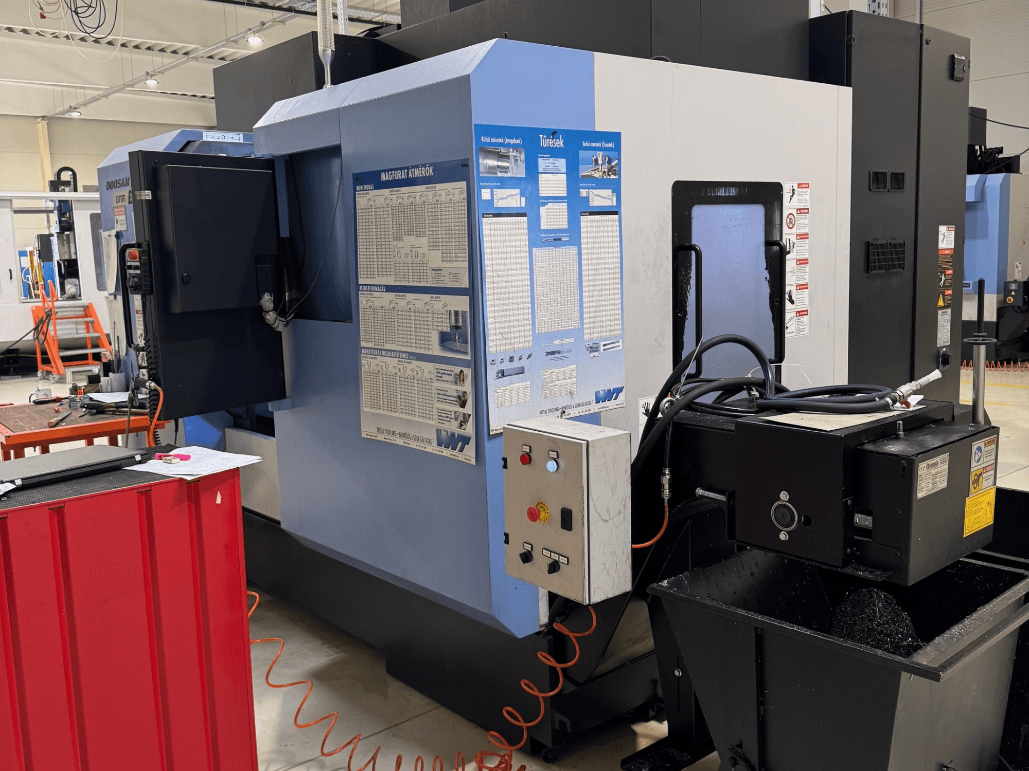 Токарно-фрезерный центр DOOSAN DNM350/5AX, вид сбоку, на котором видны панель управления и бак для охлаждающей жидкости, а также детали рабочего процесса.